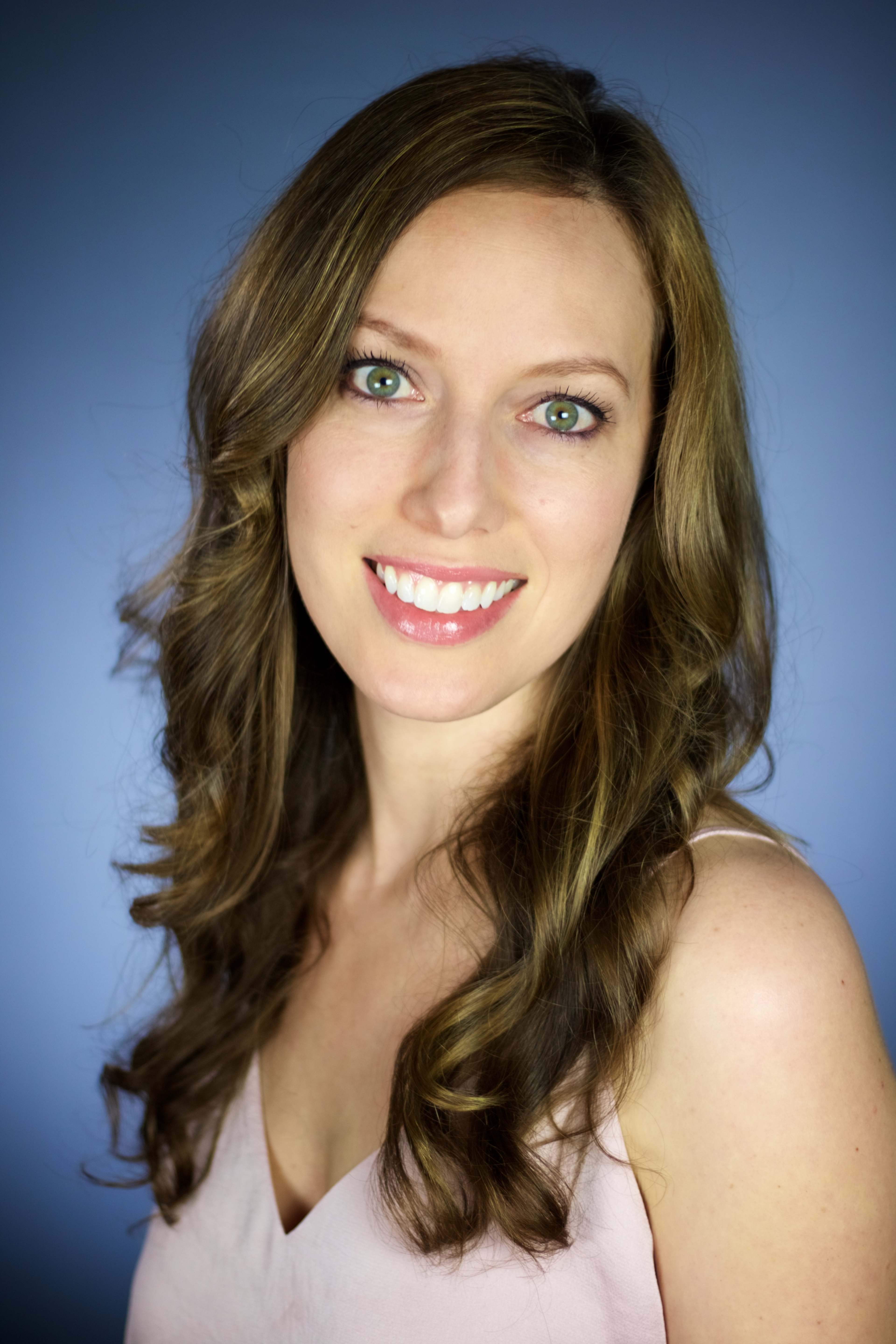 A woman with long, wavy hair smiles at the camera against a blue background.