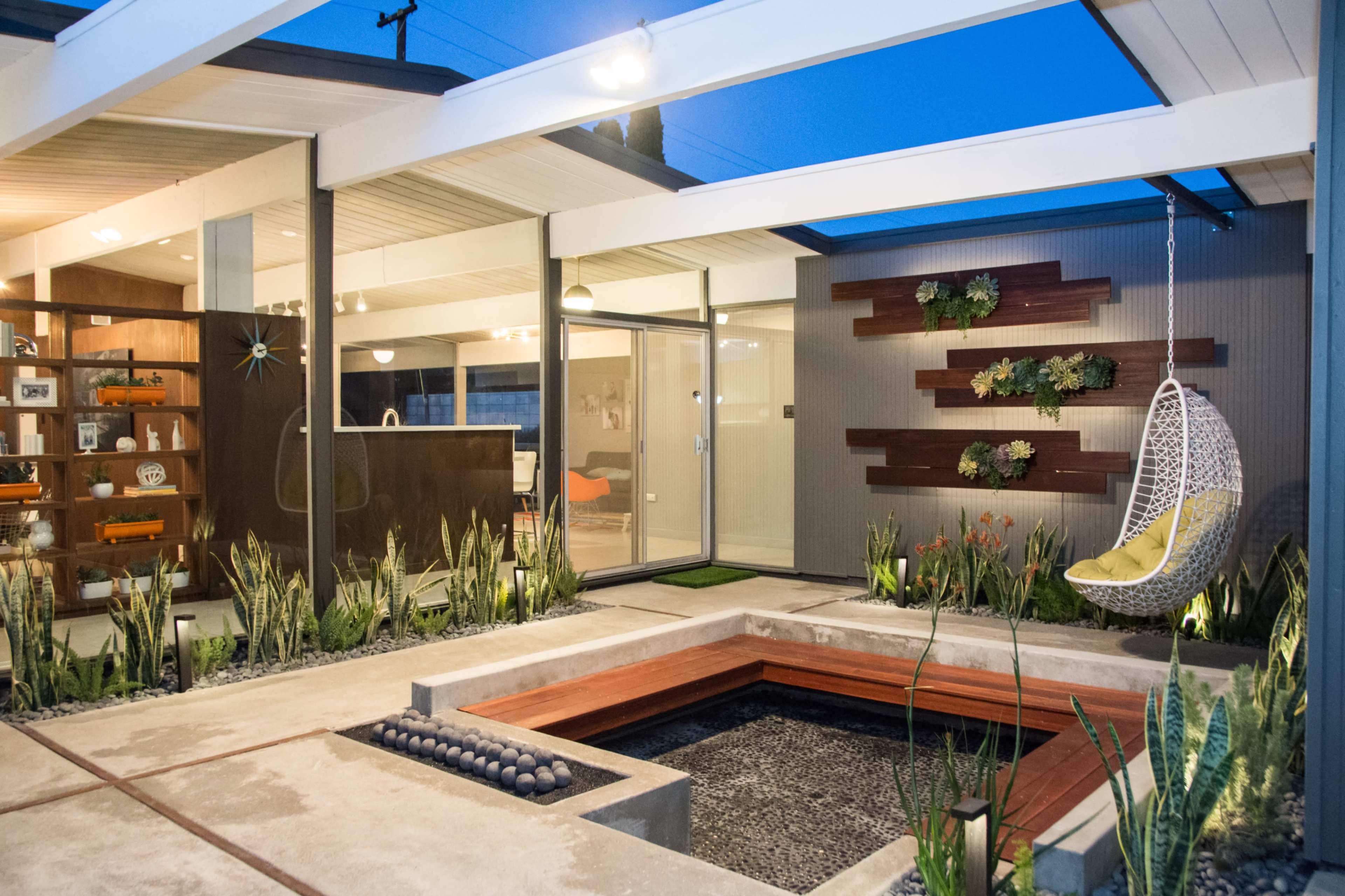 A modern courtyard featuring a gel-filled central planter, a hanging chair, and decorative plants against a sleek architectural backdrop.