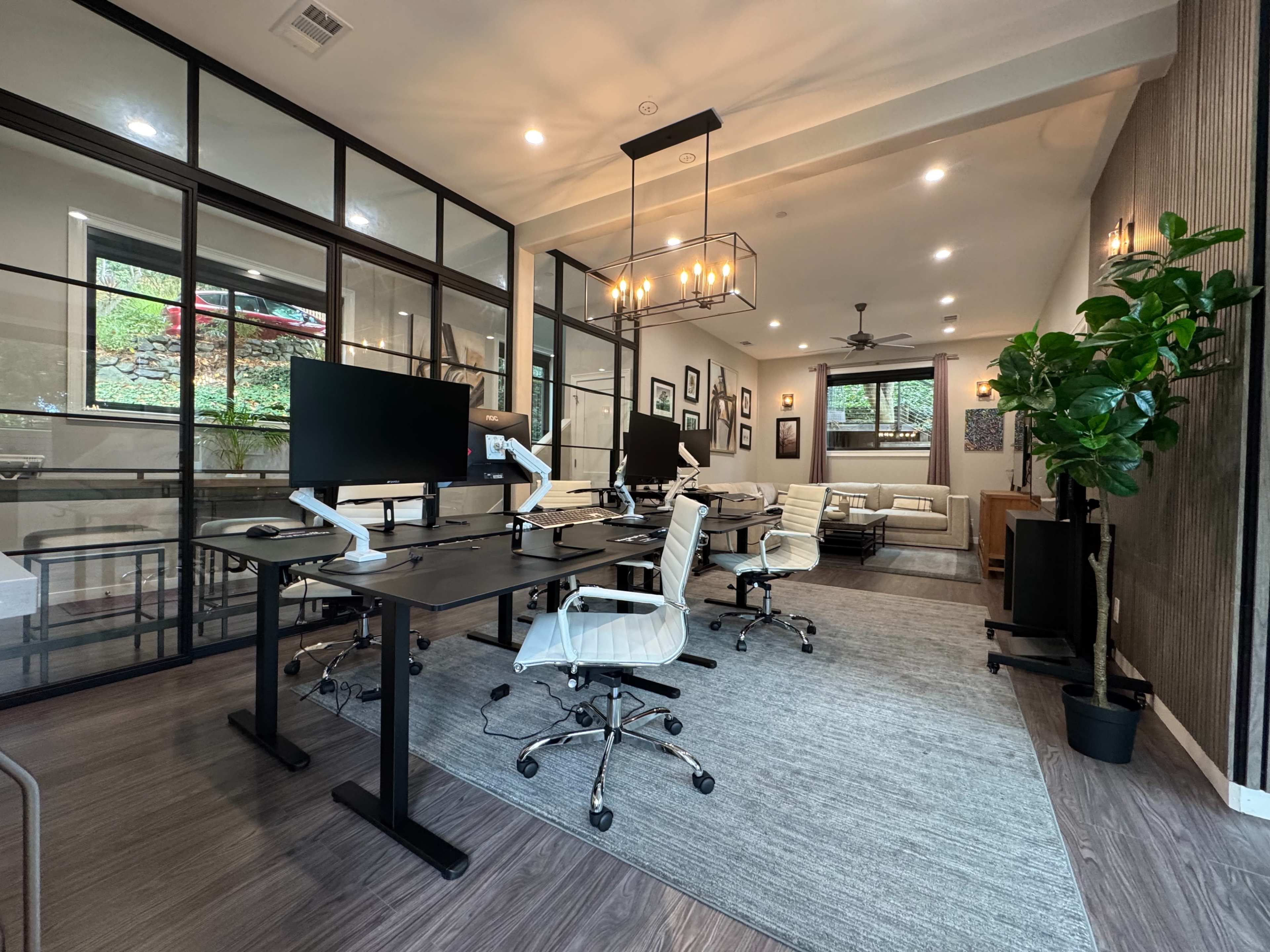 The image shows a modern office space with multiple workstations, featuring desks with computer monitors, ergonomic chairs, and a lounge area in the background.
