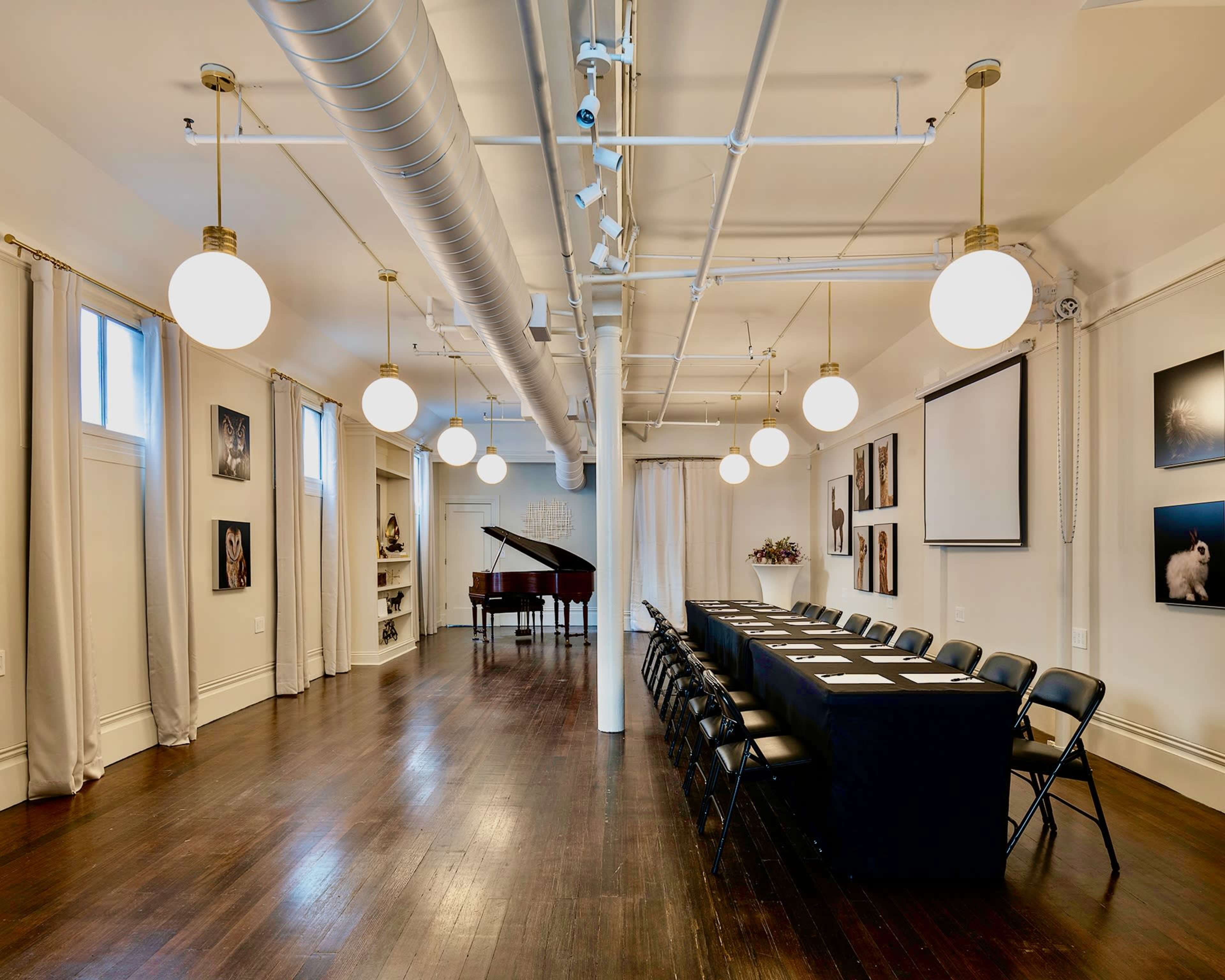 A large, well-lit conference room features a long table with chairs, a grand piano in the corner, and framed photographs on the walls.