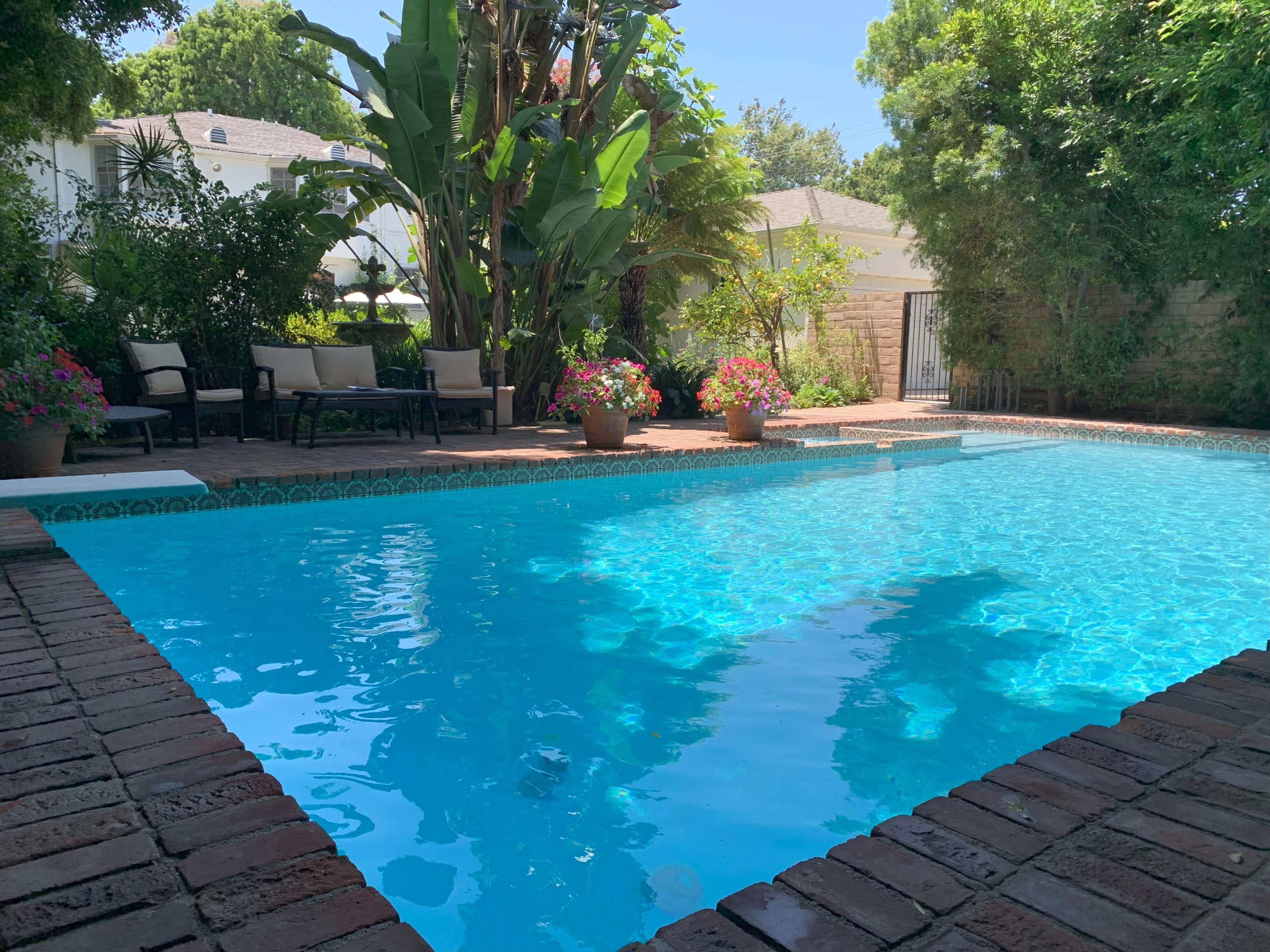 A swimming pool surrounded by brick coping, with potted plants and seating areas located around the pool.