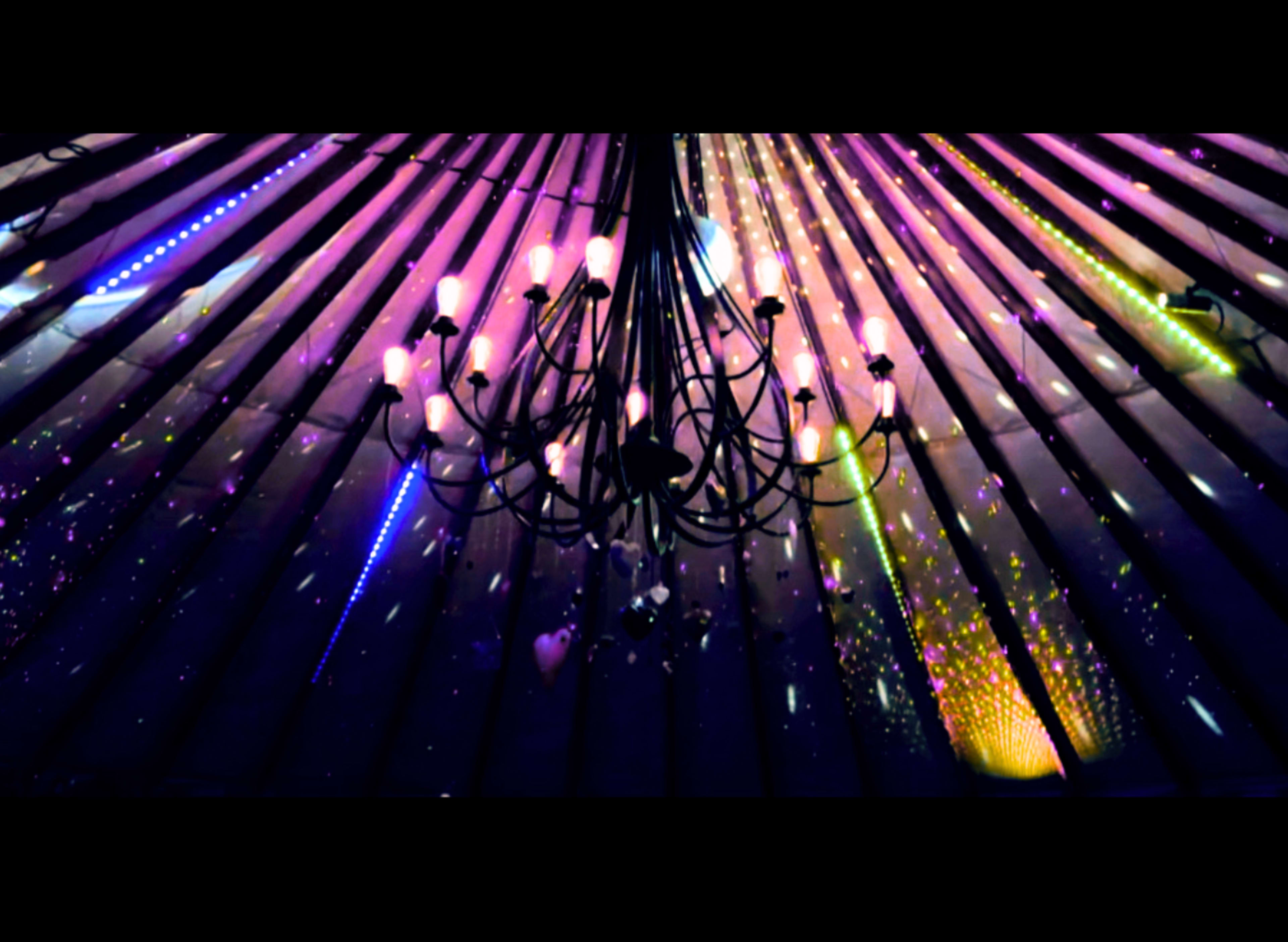 A chandelier hangs from the ceiling beneath a vibrant, multicolored light display.