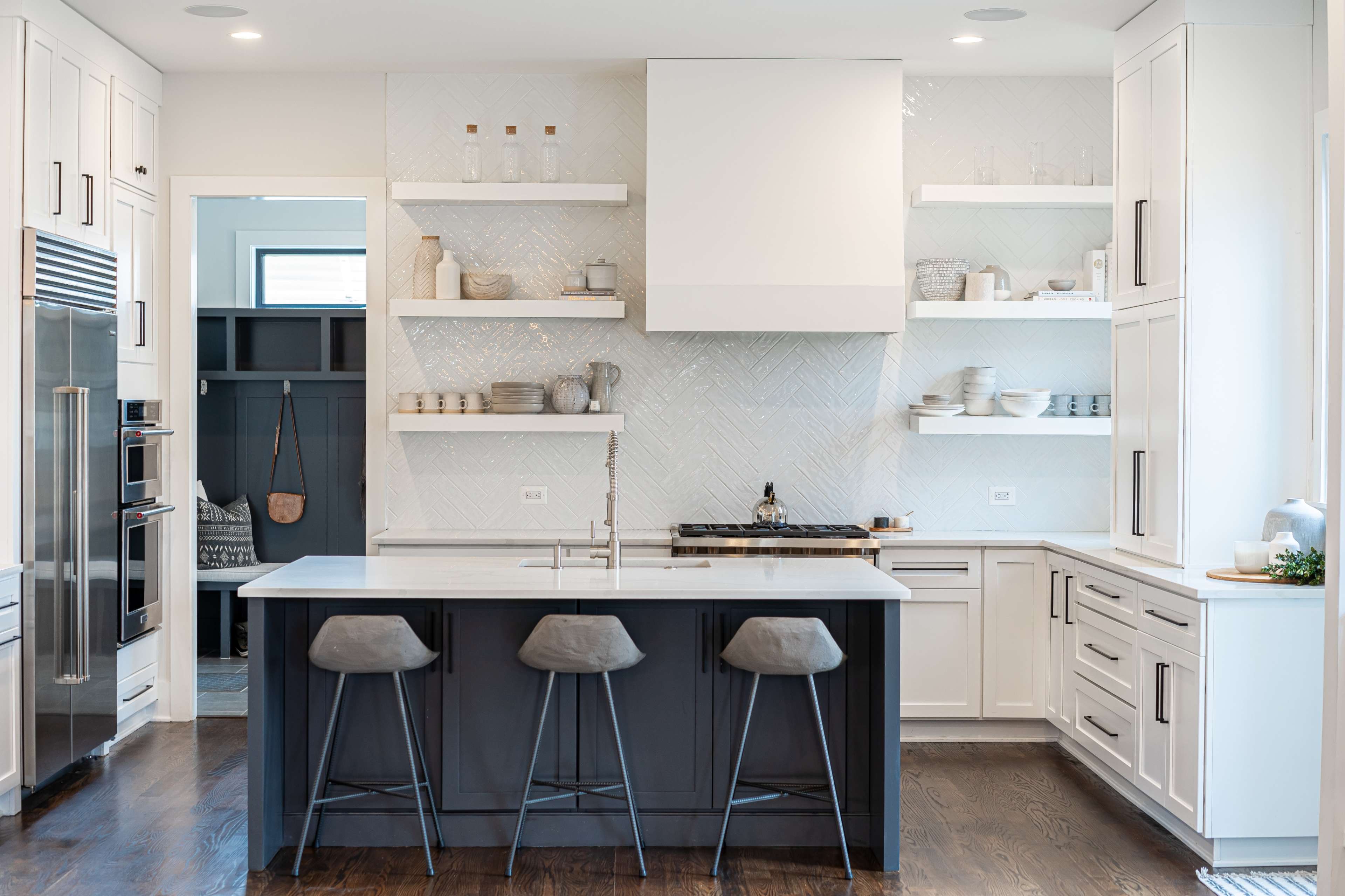 A modern kitchen features a large island with three stools, white cabinetry, open shelving, and contrasting dark cabinetry.