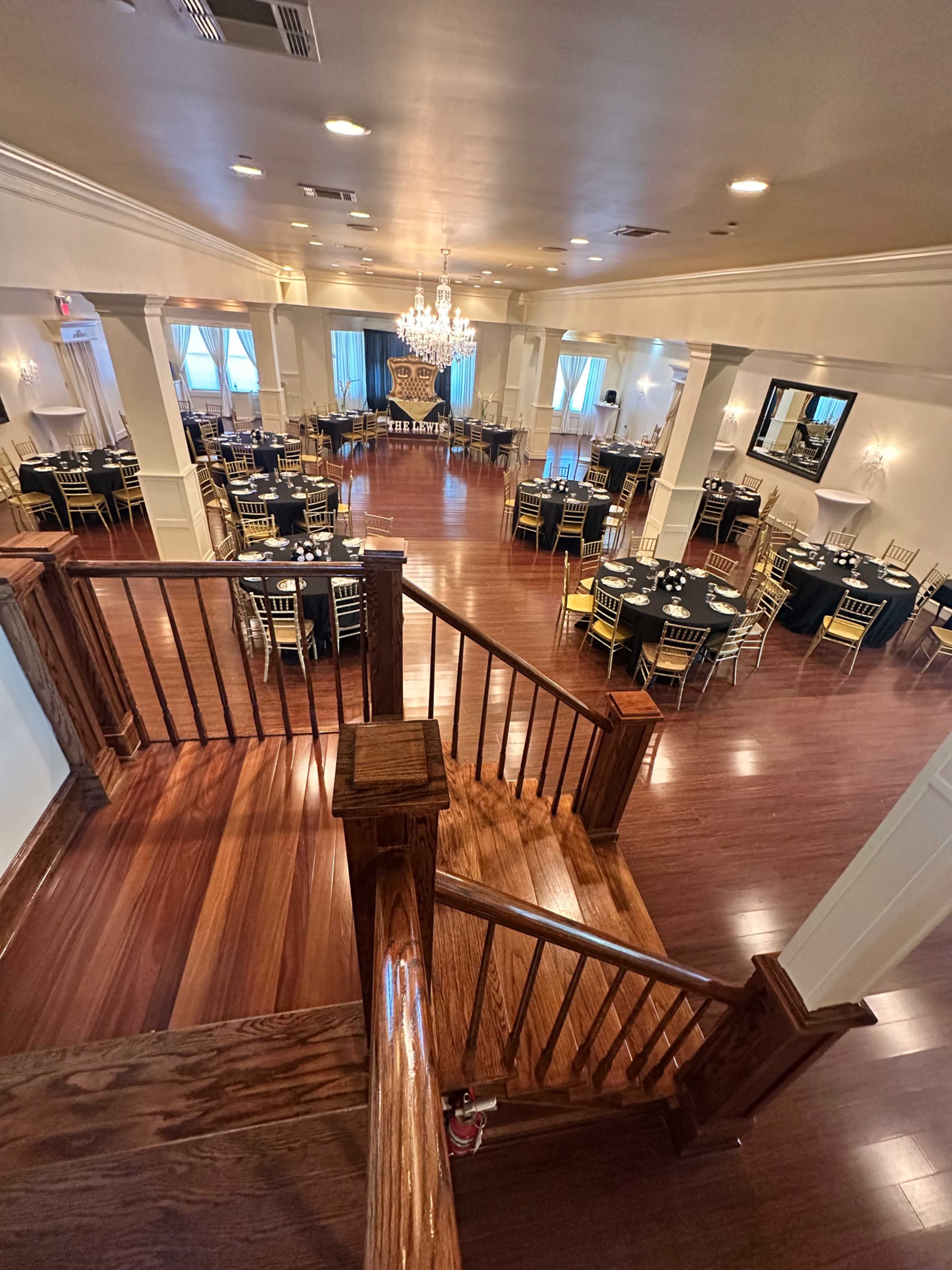 The image shows a spacious banquet hall with polished wooden floors, elegant chandeliers, and tables set for dining.