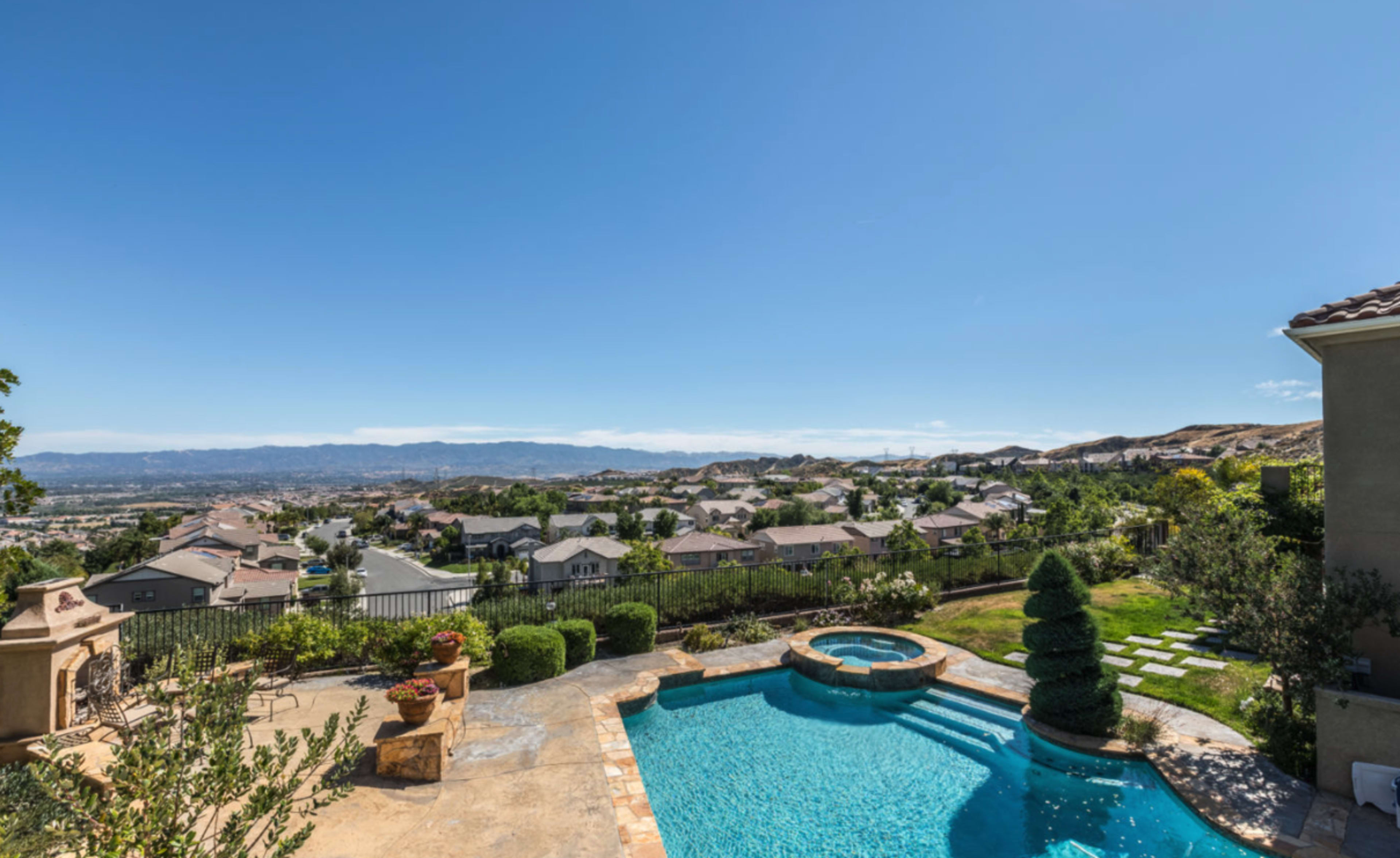 This image shows a backyard with a swimming pool overlooking a residential area and a mountainous landscape in the distance.