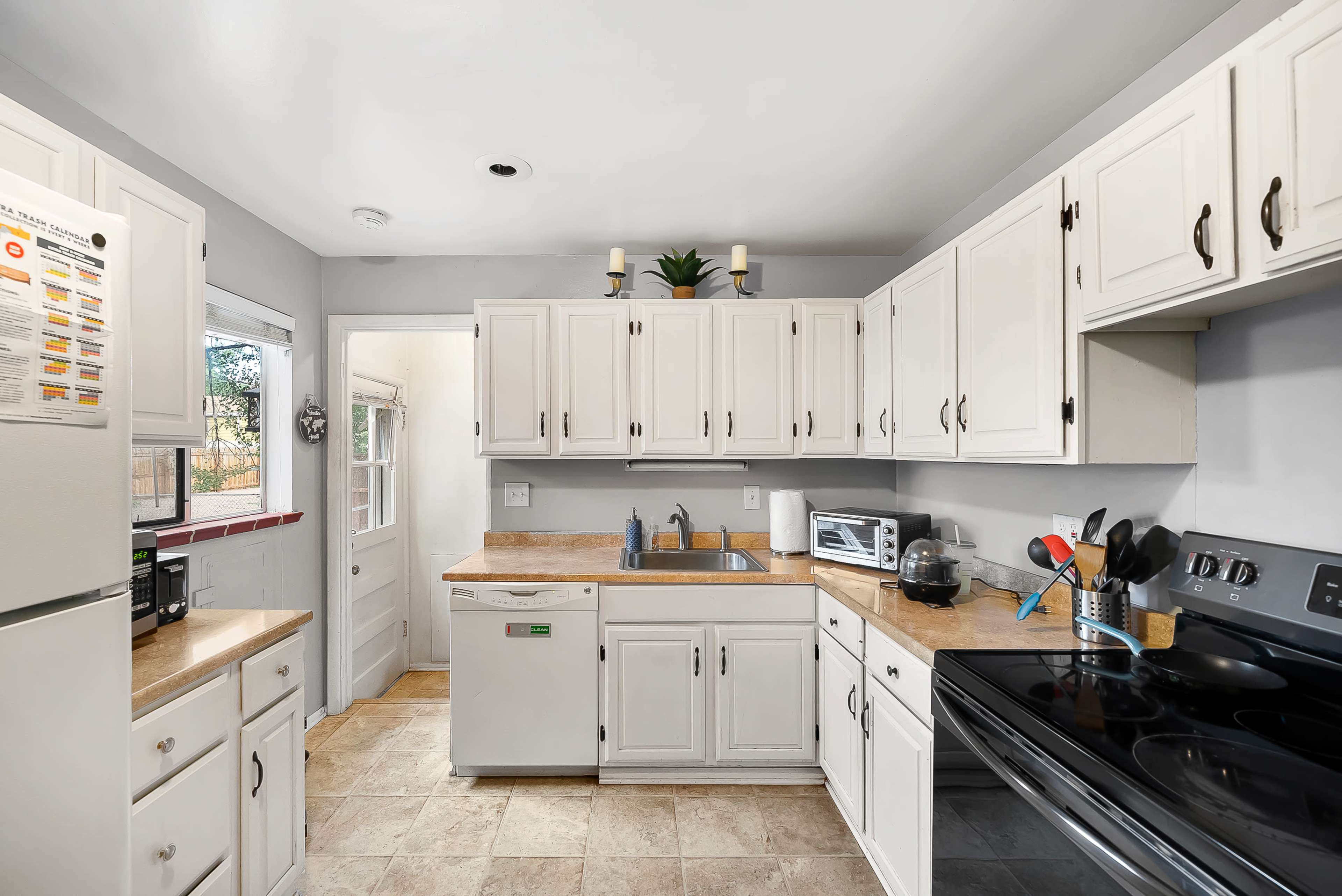 The image shows a small kitchen featuring white cabinets, a black stove, and a sink with countertop space, along with appliances like a microwave and a dishwasher.