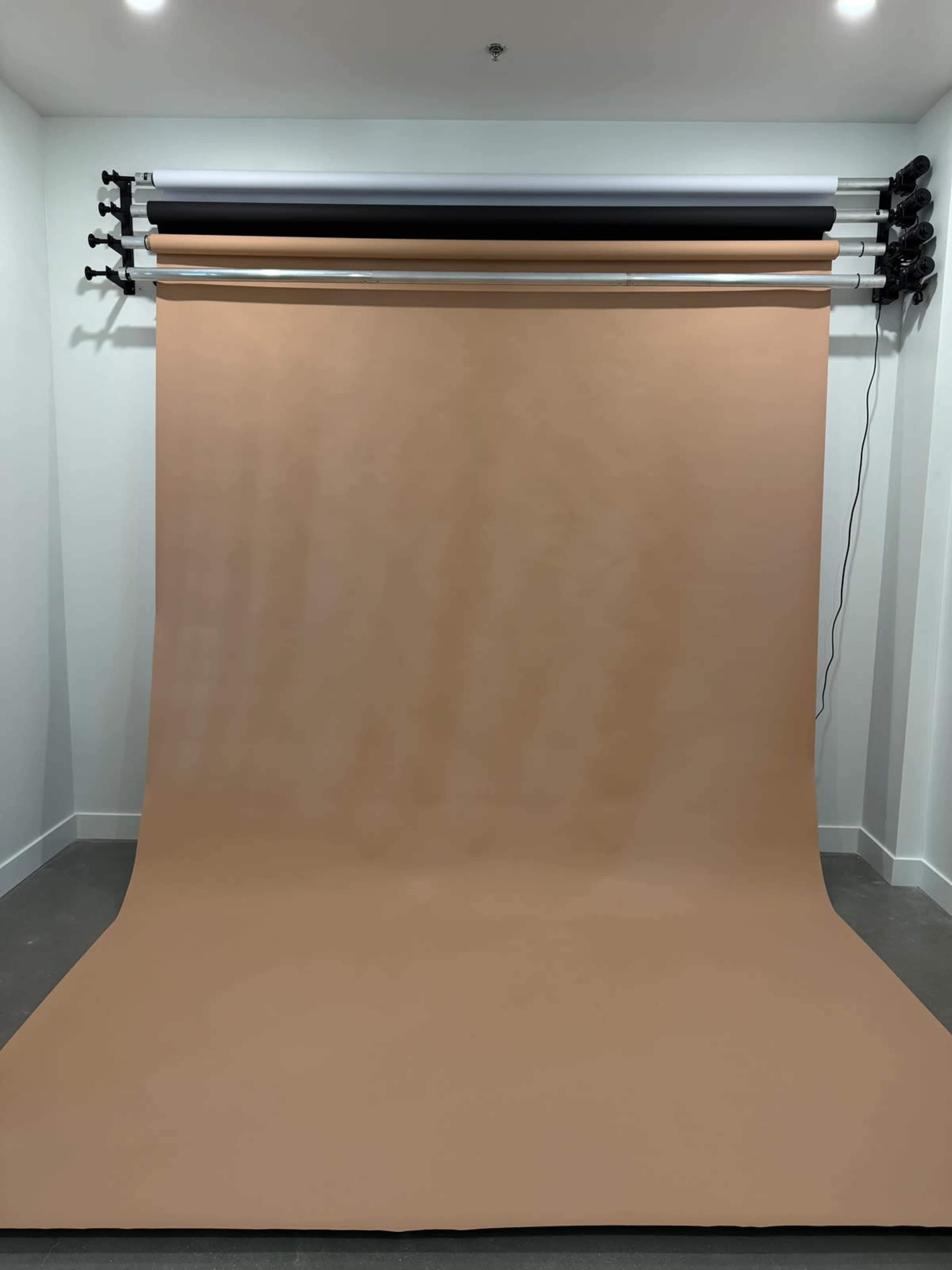 The image shows a photography studio with a large roll of brown backdrop paper hanging from a rack on the wall, extending onto the floor.