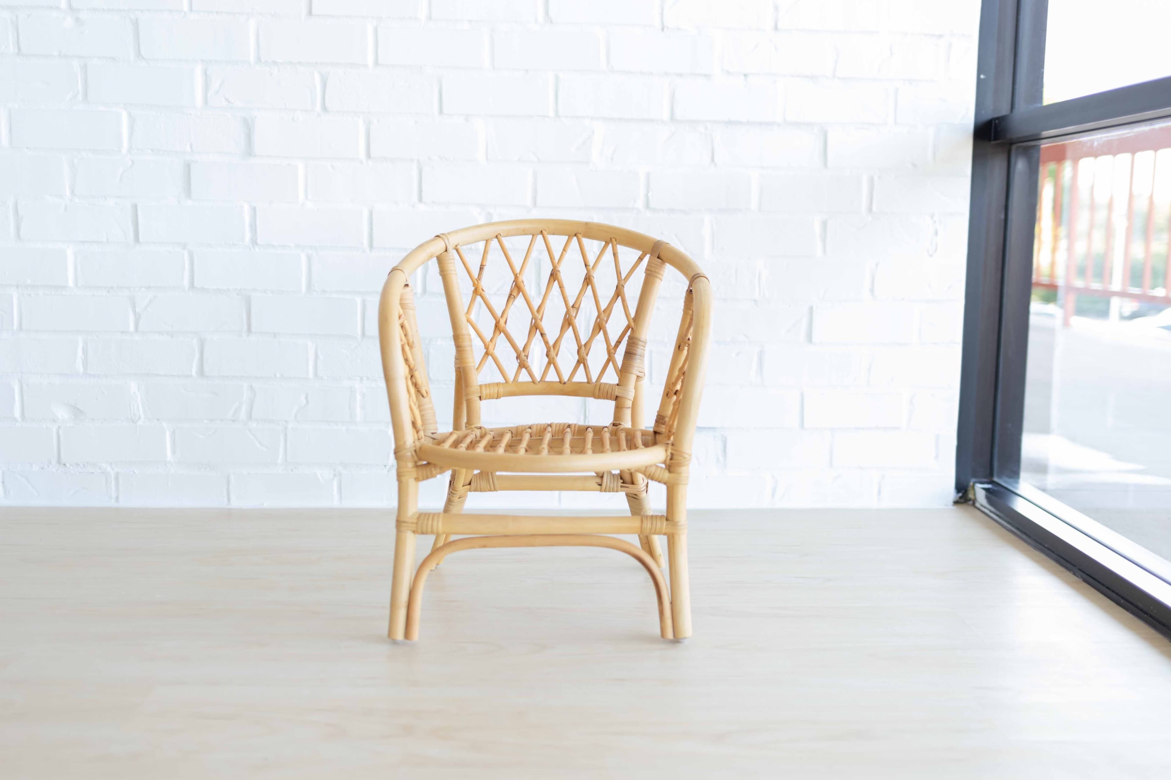 A woven rattan chair is positioned against a white brick wall near a large window.