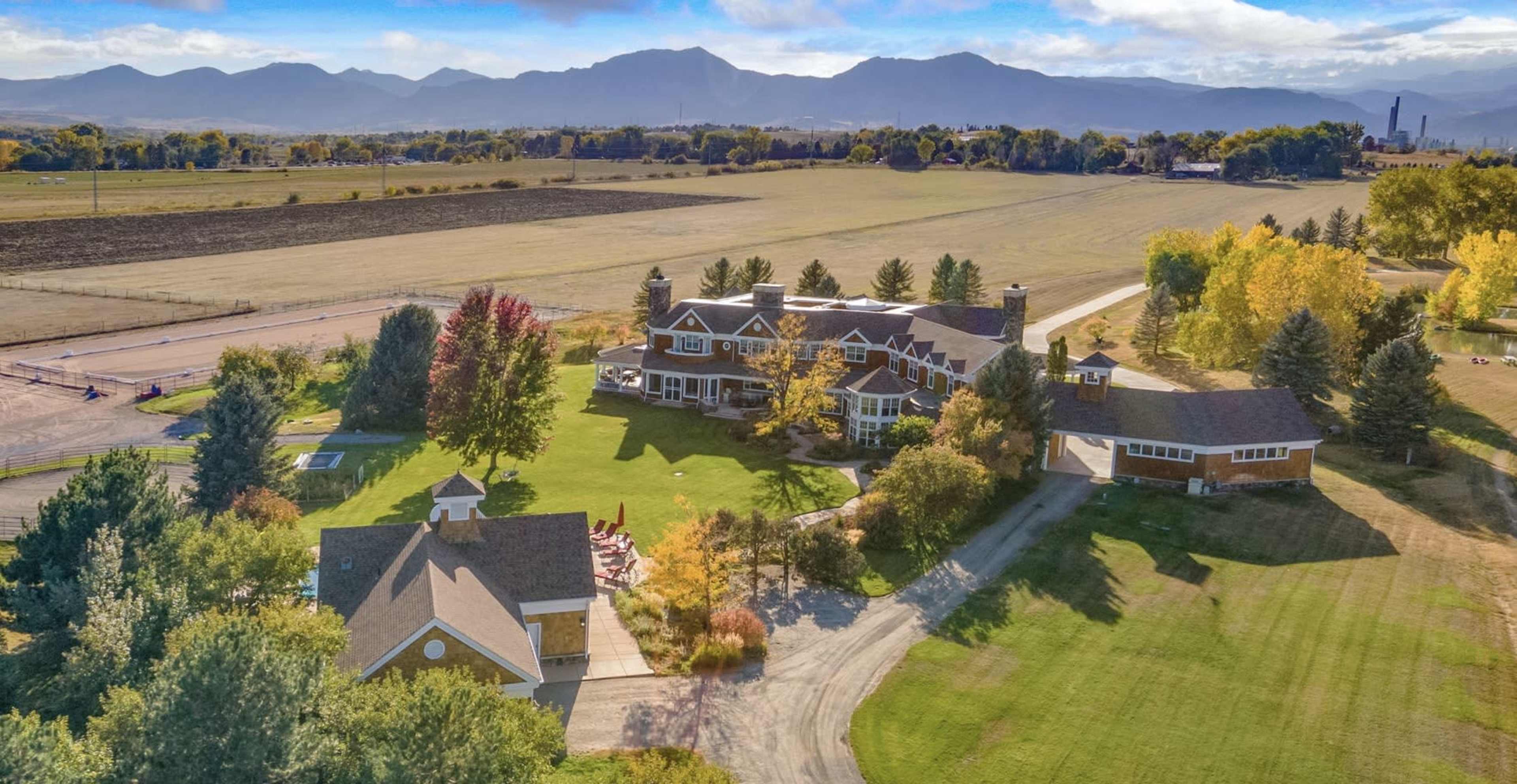 The image shows a large estate with several buildings and well-maintained grounds, surrounded by fields and mountains in the background.