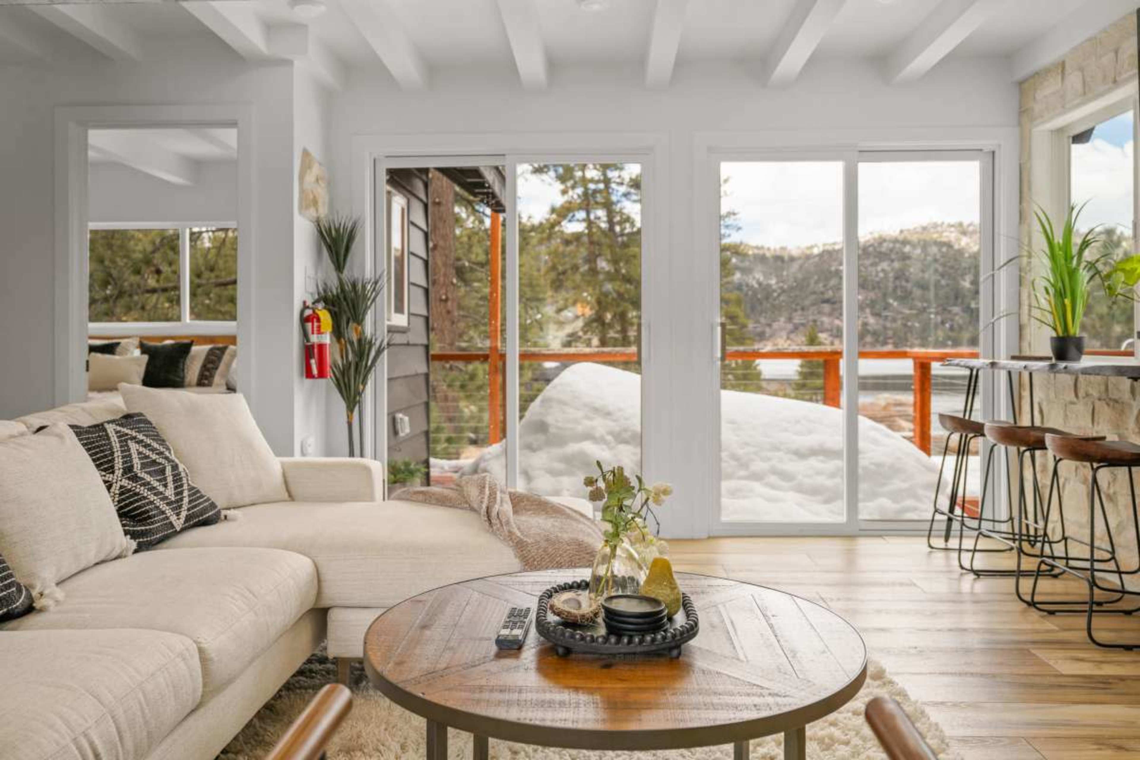 The image shows a cozy living room with a beige sofa, a wooden coffee table, and large windows overlooking a snowy landscape.