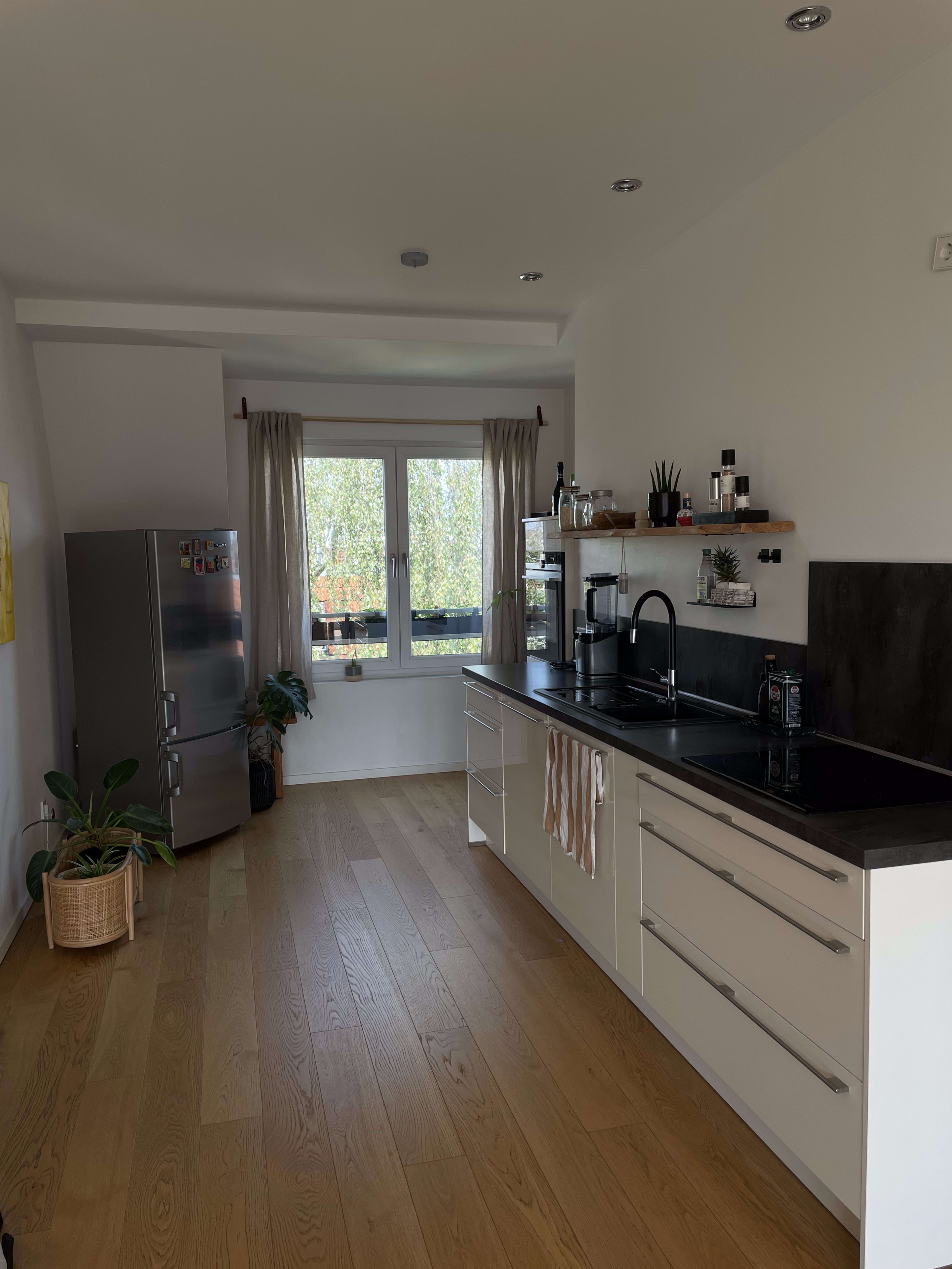 A modern kitchen features sleek cabinetry, a black countertop, and large windows with natural light filling the space.