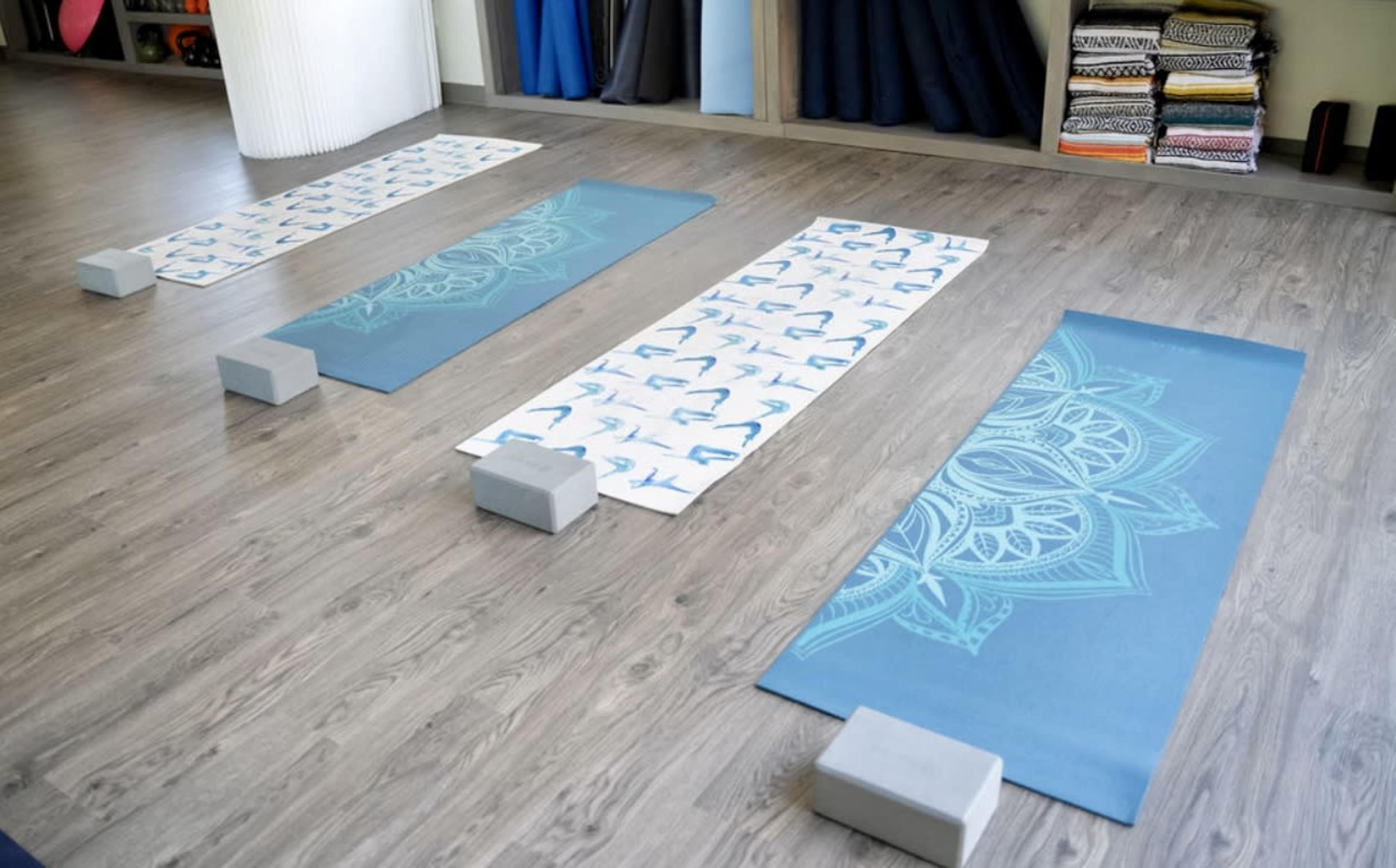 The image shows a yoga studio with four exercise mats arranged on a wooden floor, accompanied by gray yoga blocks.