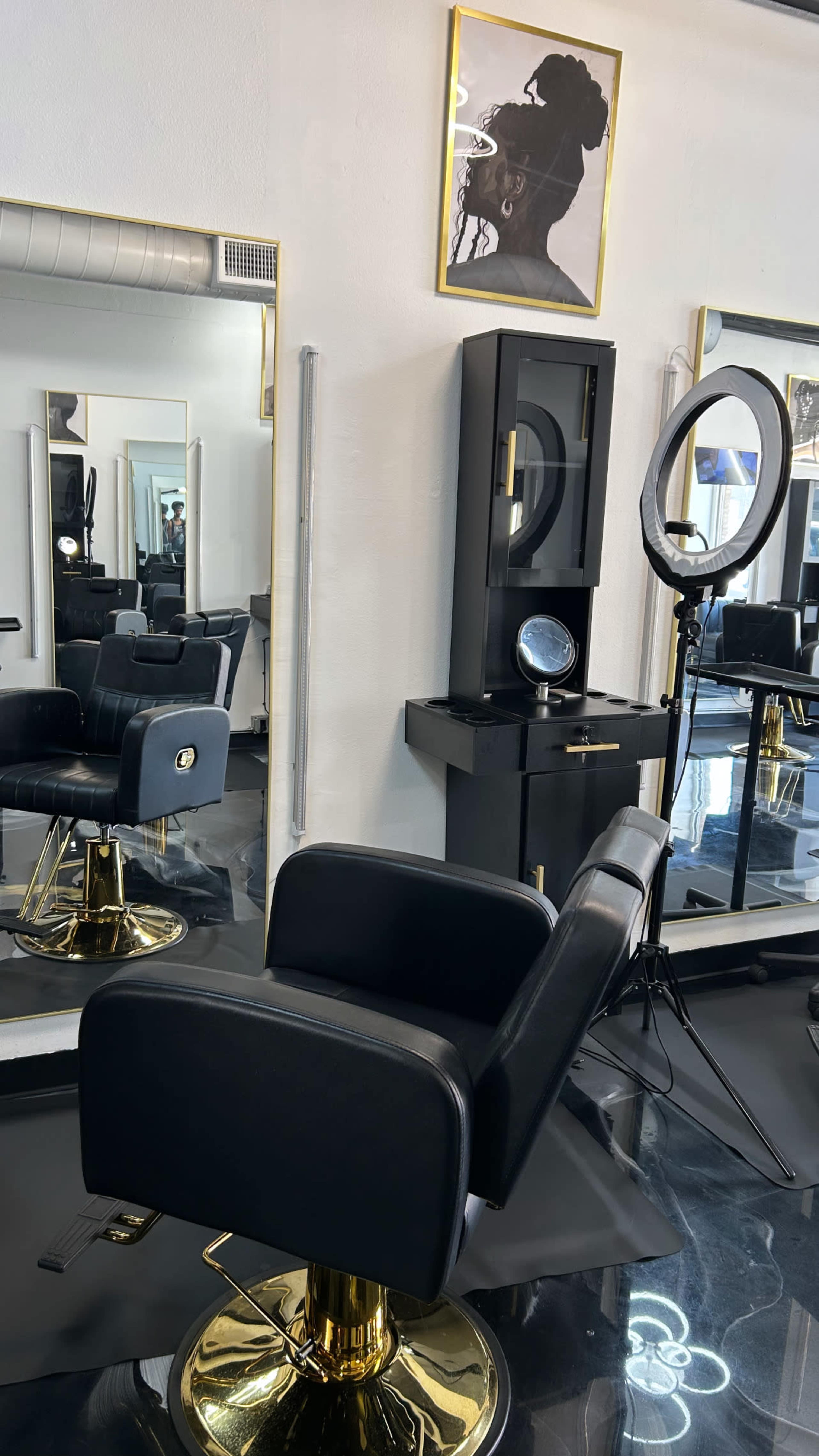 The image shows a modern hair salon with black leather styling chairs, mirrors, and a ring light setup, featuring a portrait on the wall.