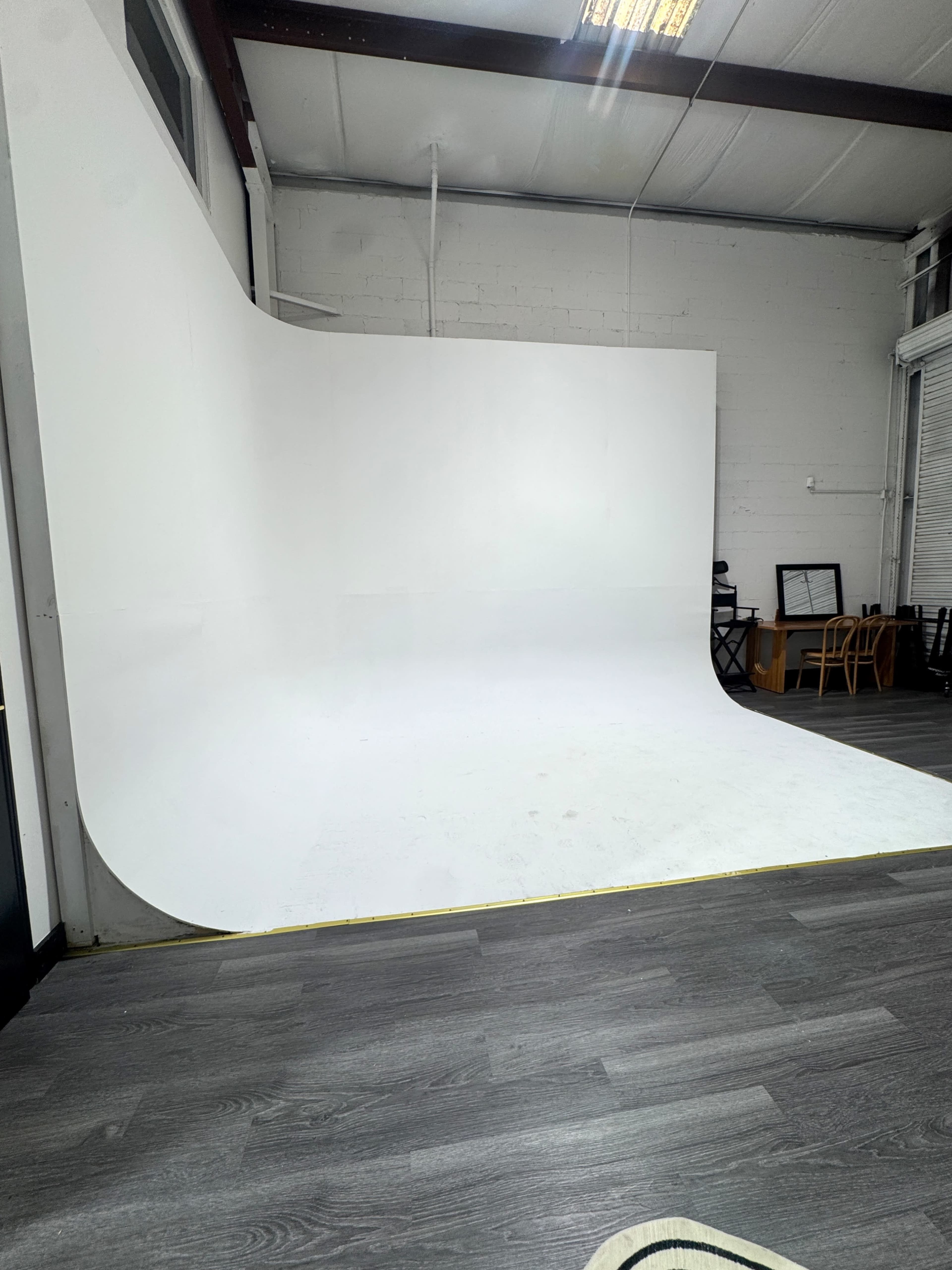 The image shows a spacious photography studio with a large white backdrop and wooden flooring.