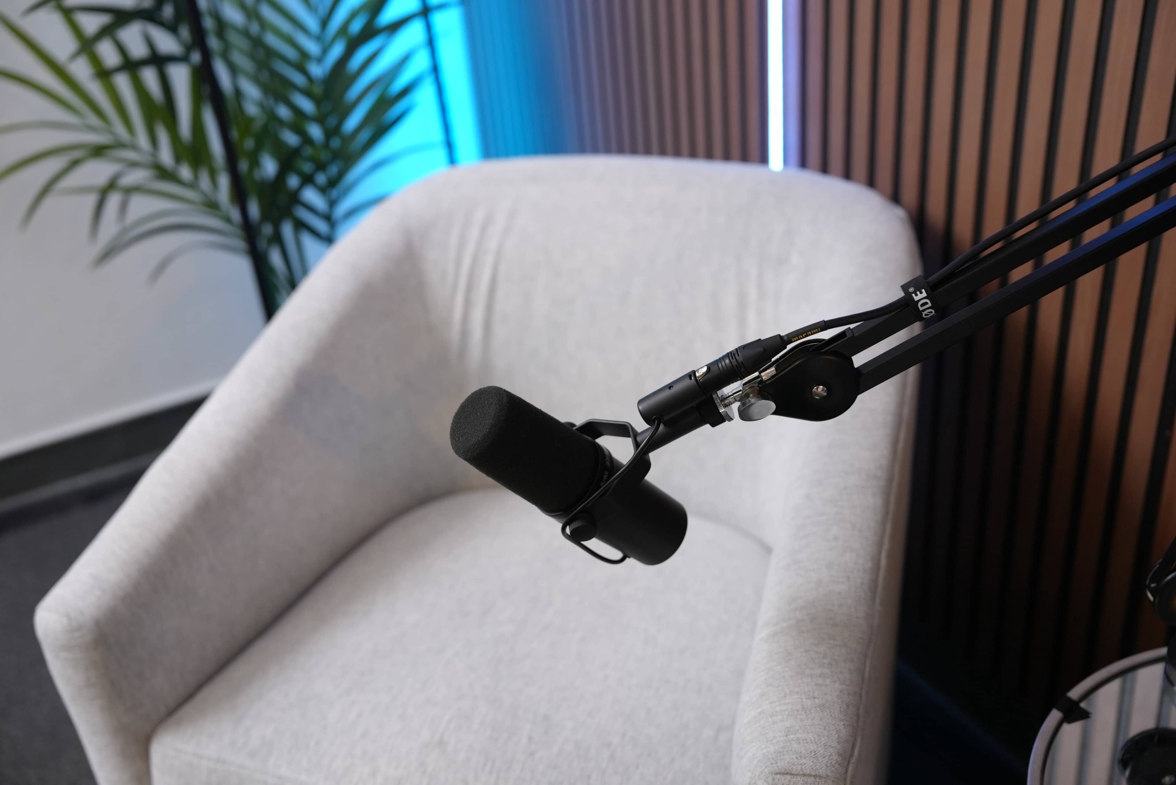 A microphone is positioned on a boom arm above a gray armchair in a studio setup.