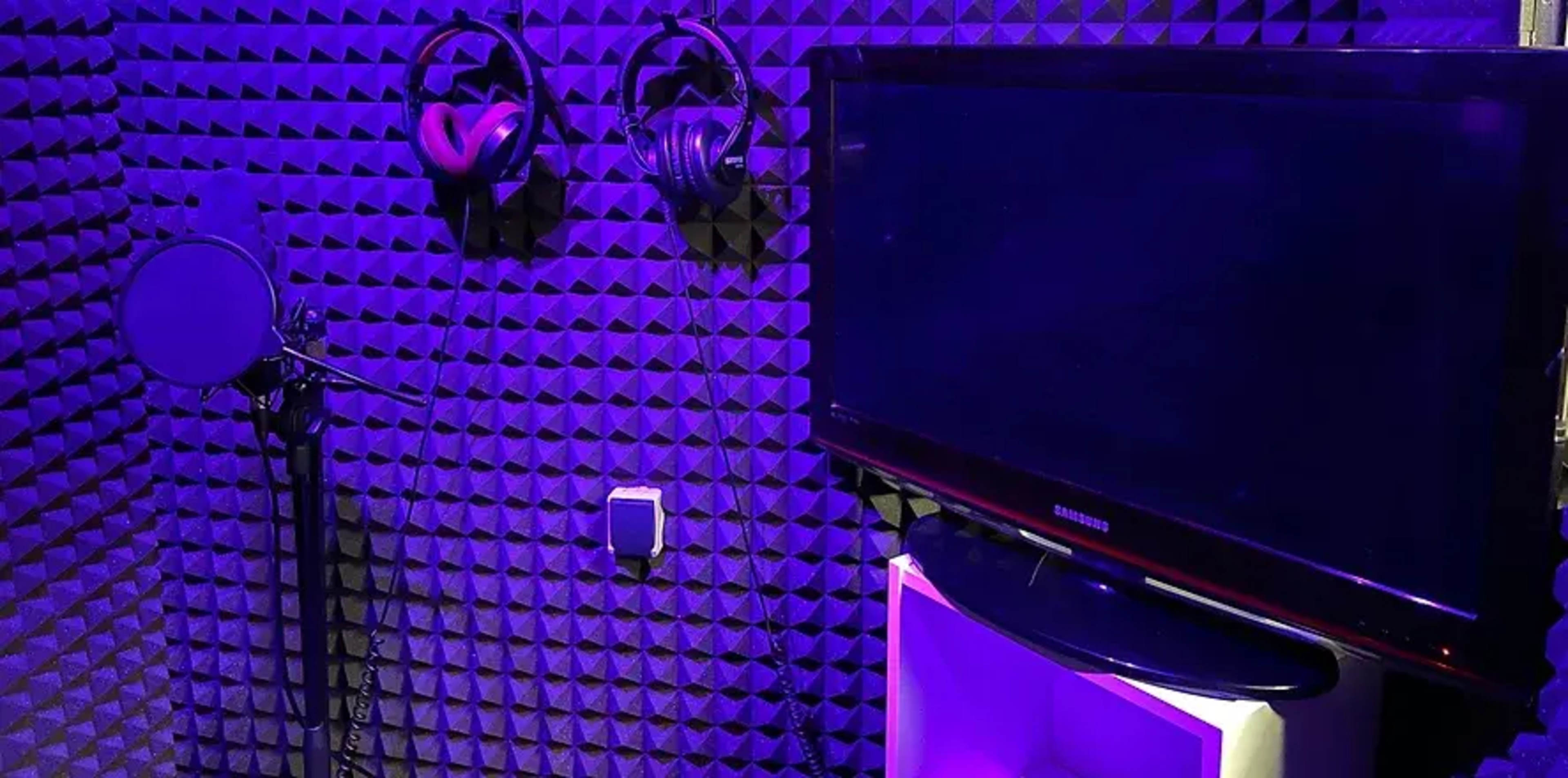 A soundproof recording studio with a microphone, headphones mounted on the wall, and a television on a stand.