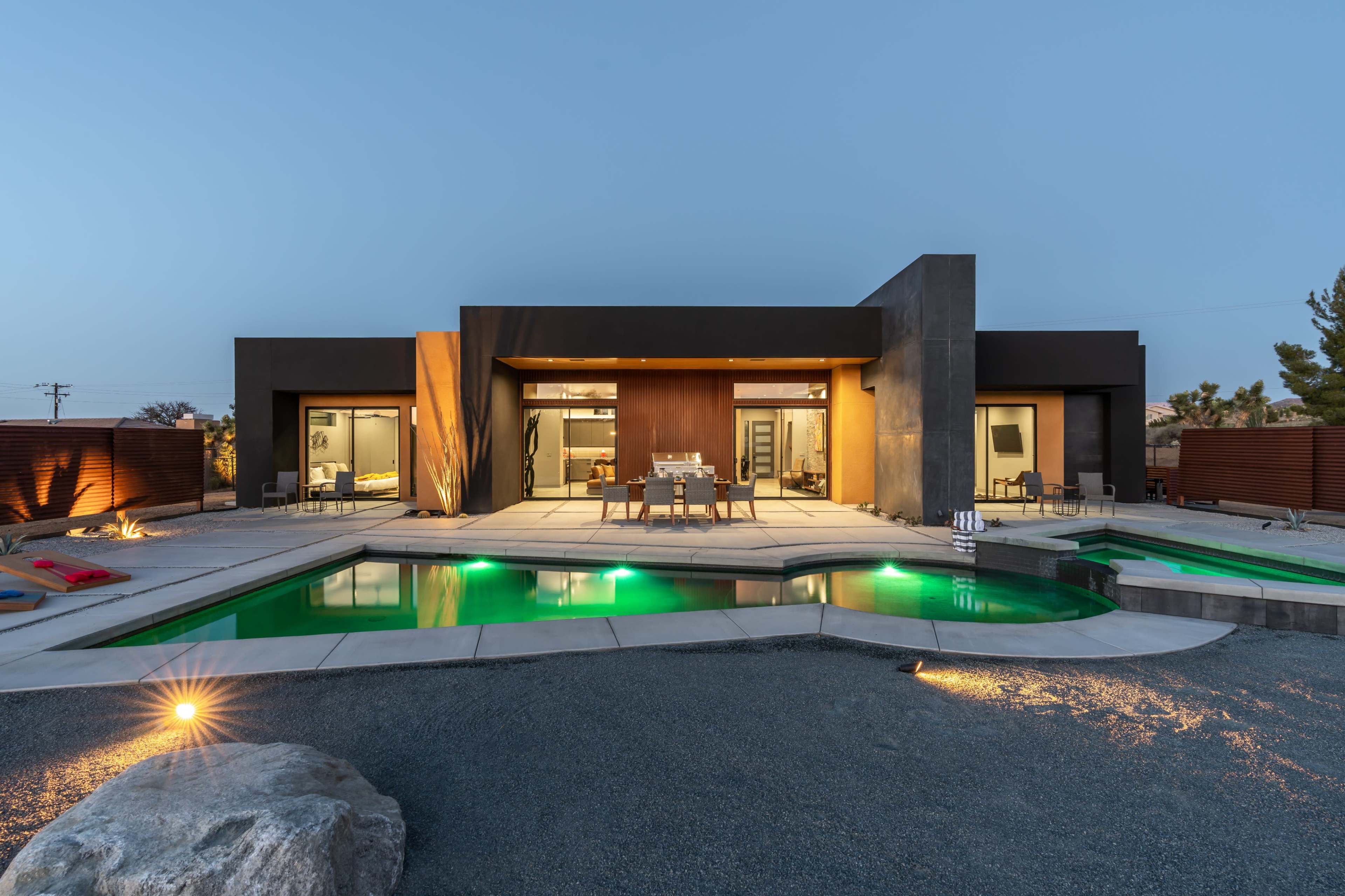 A modern house with a sleek design features large windows, a swimming pool, and outdoor seating illuminated by soft lighting.