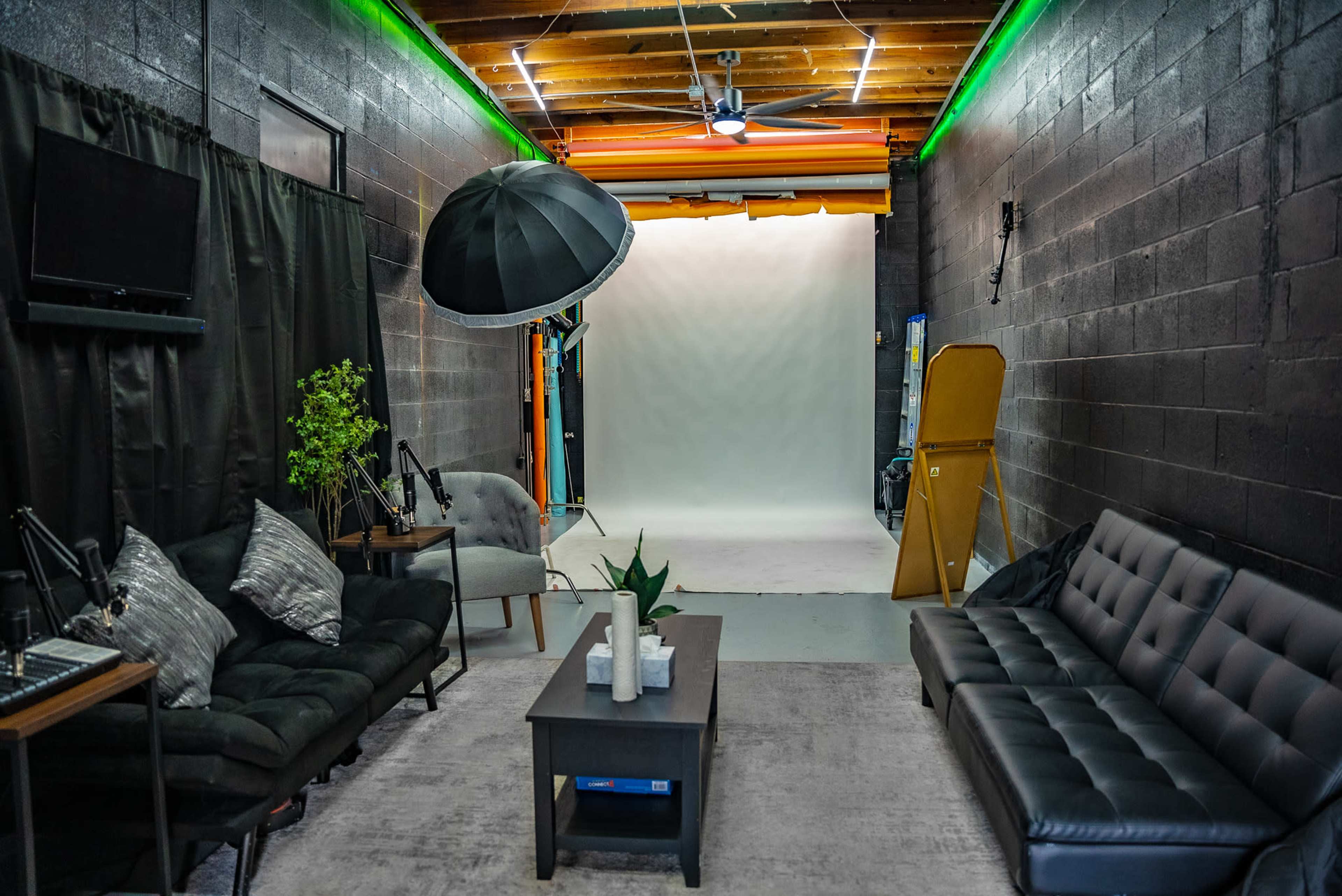 A photography studio featuring a neutral backdrop, seating area with two couches, and equipment including a large umbrella light.