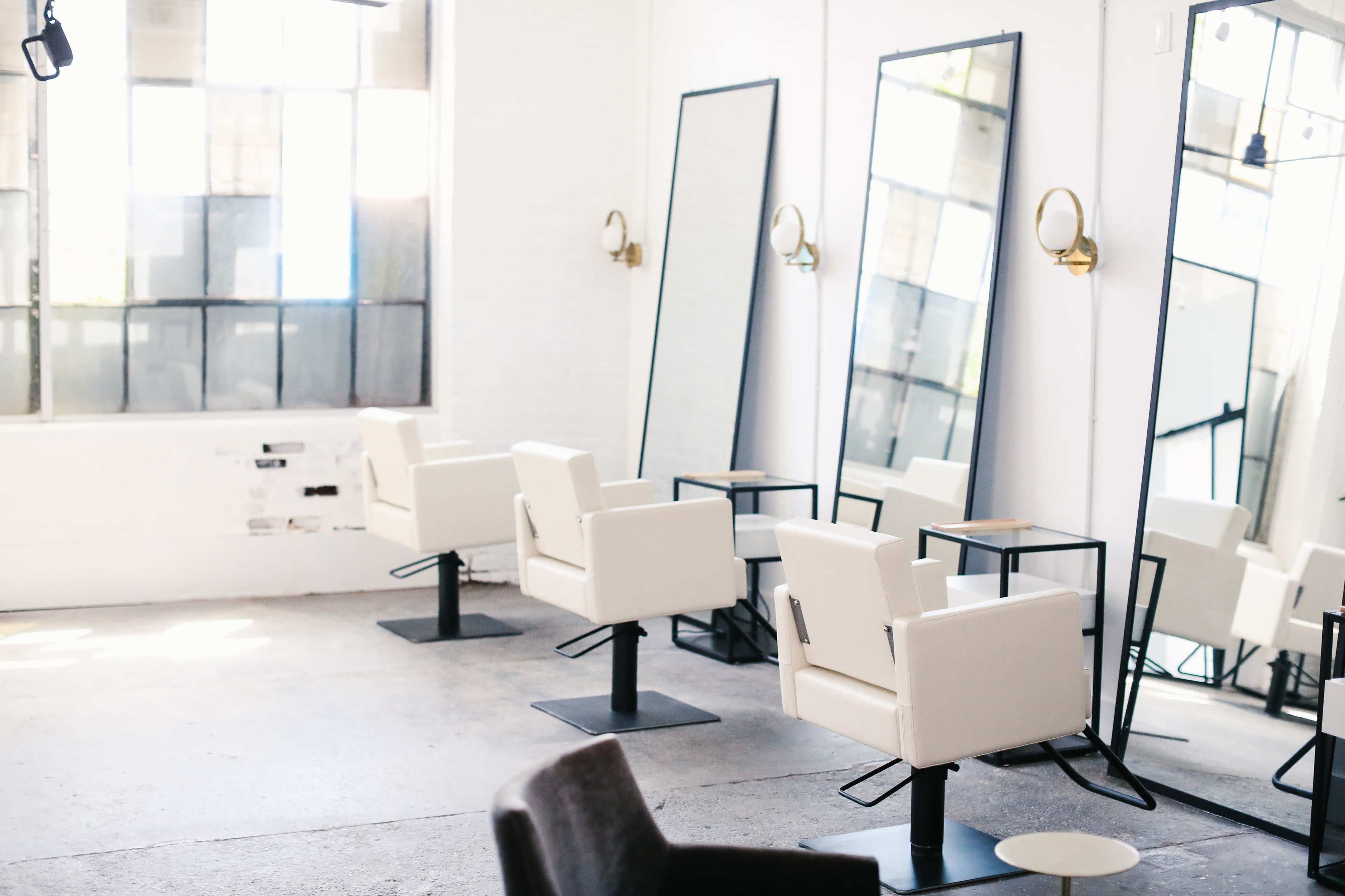 A bright hair salon with several white chairs and large mirrors along the walls.