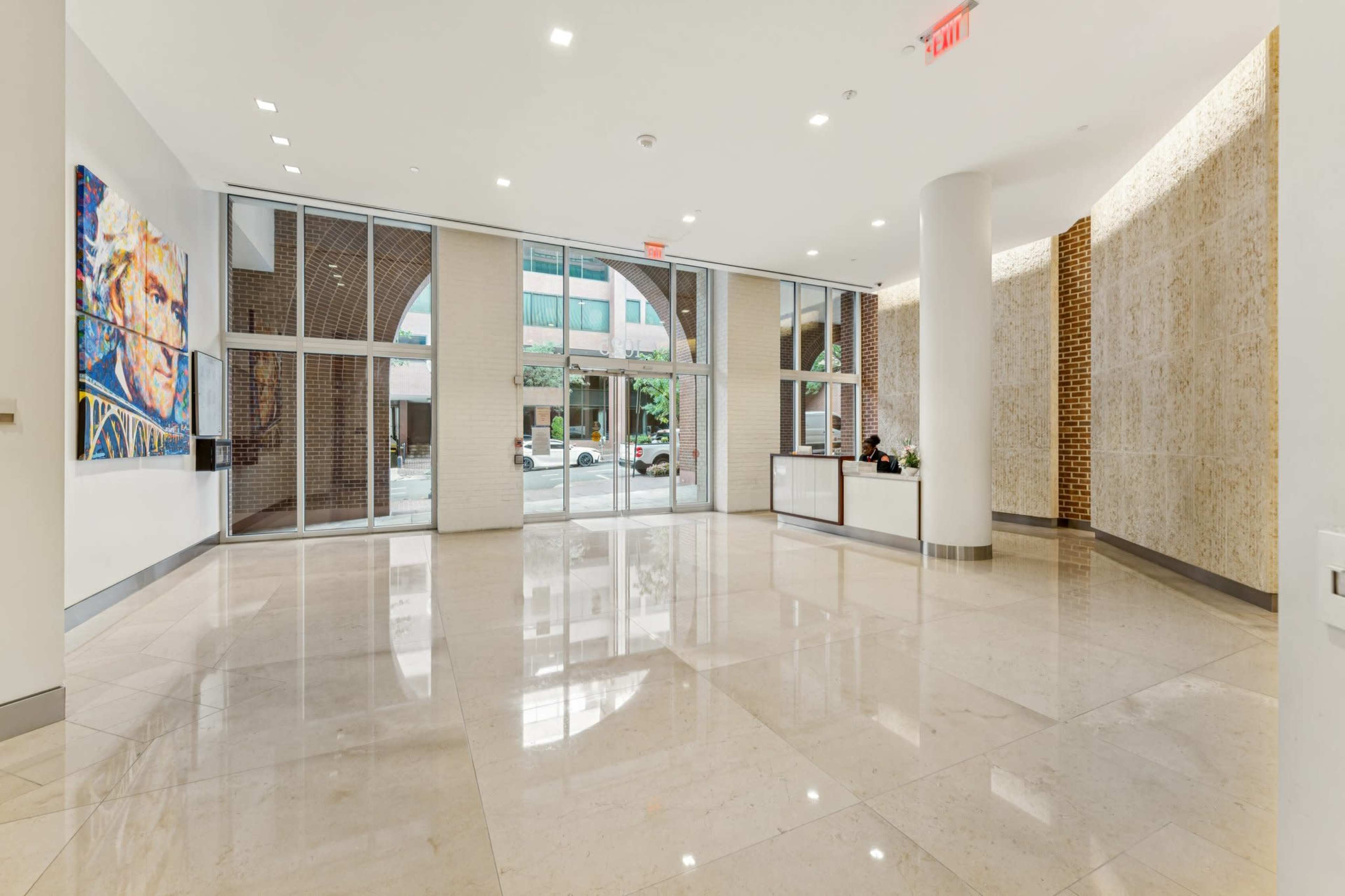 The image shows the interior of a modern lobby with a spacious marble floor, large glass windows, and contemporary artwork on the walls.