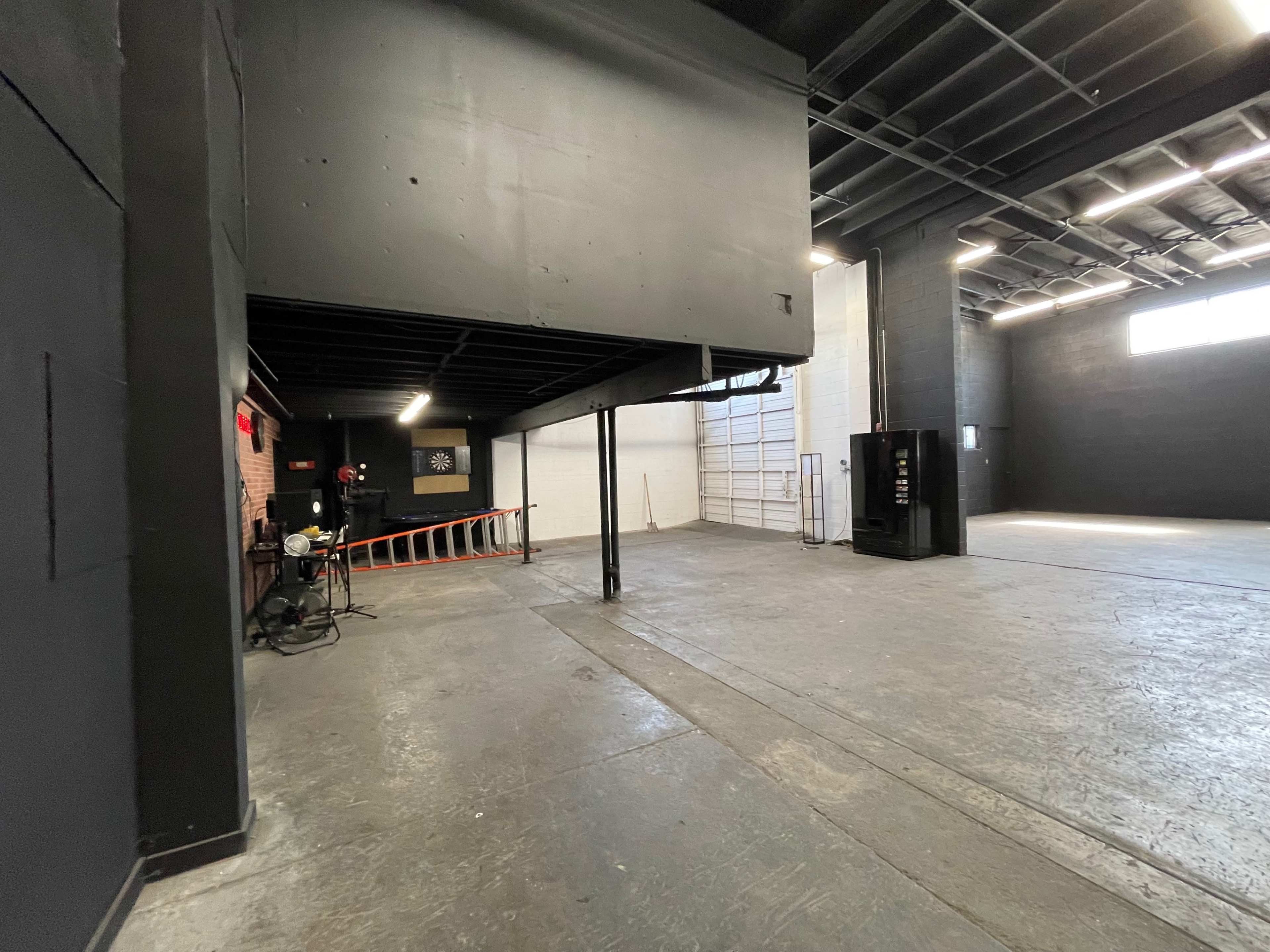 The image shows a spacious industrial interior with black walls, a raised area on the left, and a large, empty space to the right.