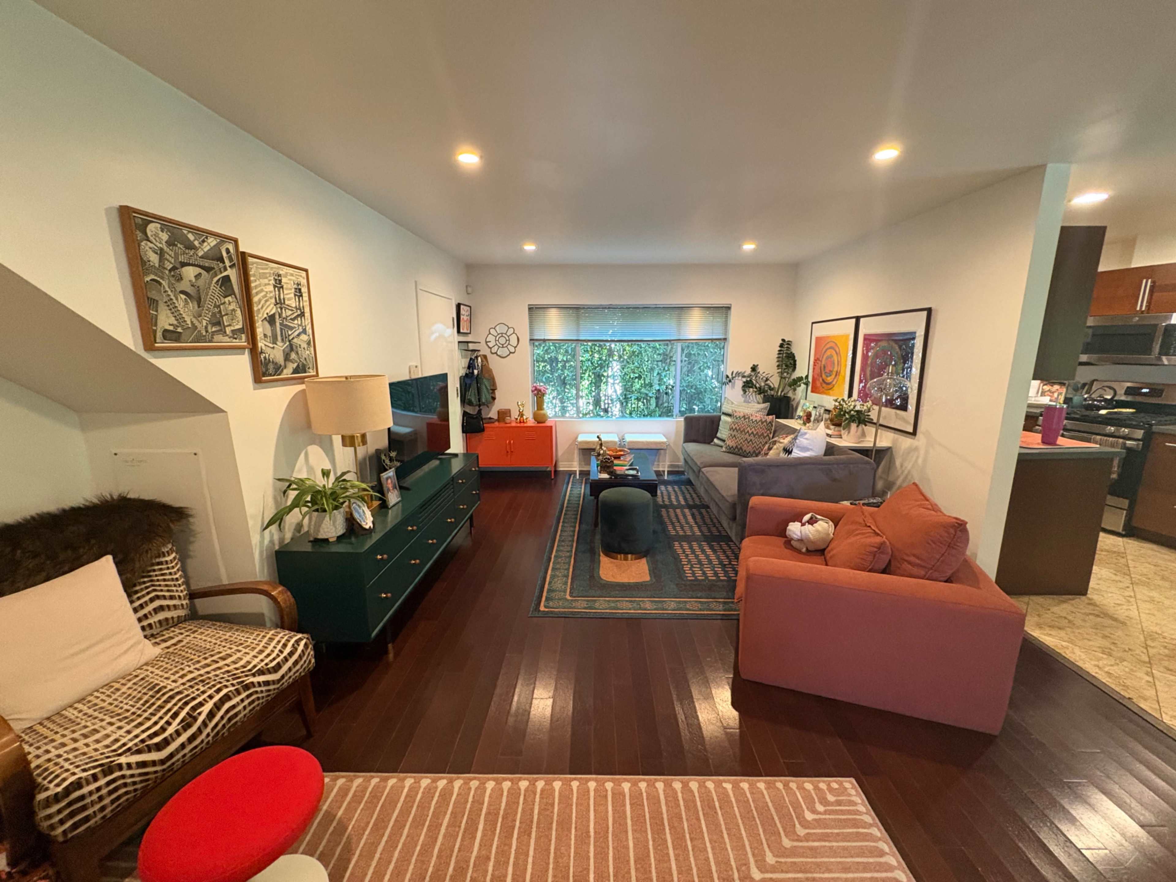 The image shows a modern living room with two sofas, a coffee table, and various decorative elements, along with a small dining area visible in the background.