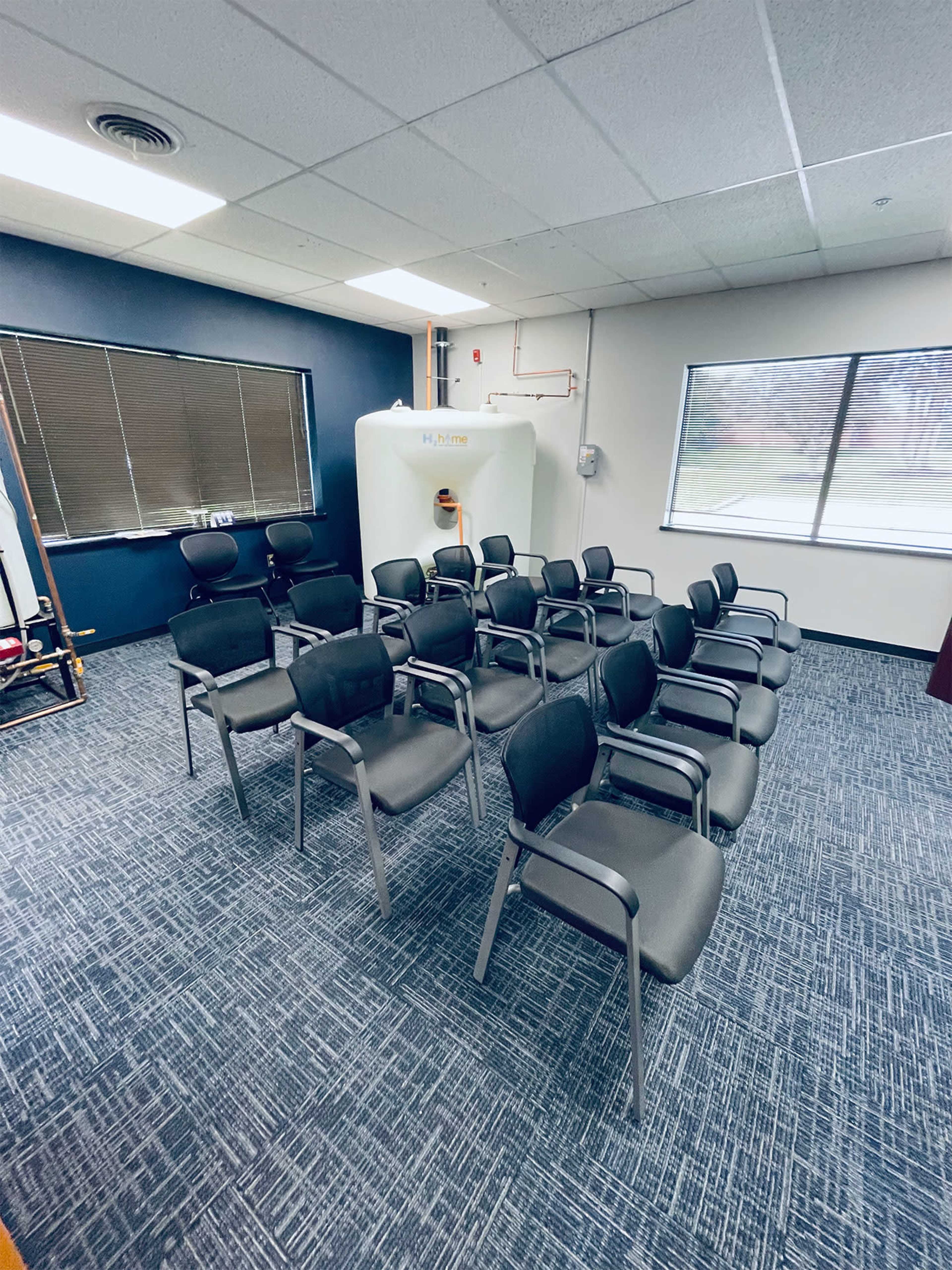 A waiting room with several rows of black chairs arranged in front of a large white machine and a window.