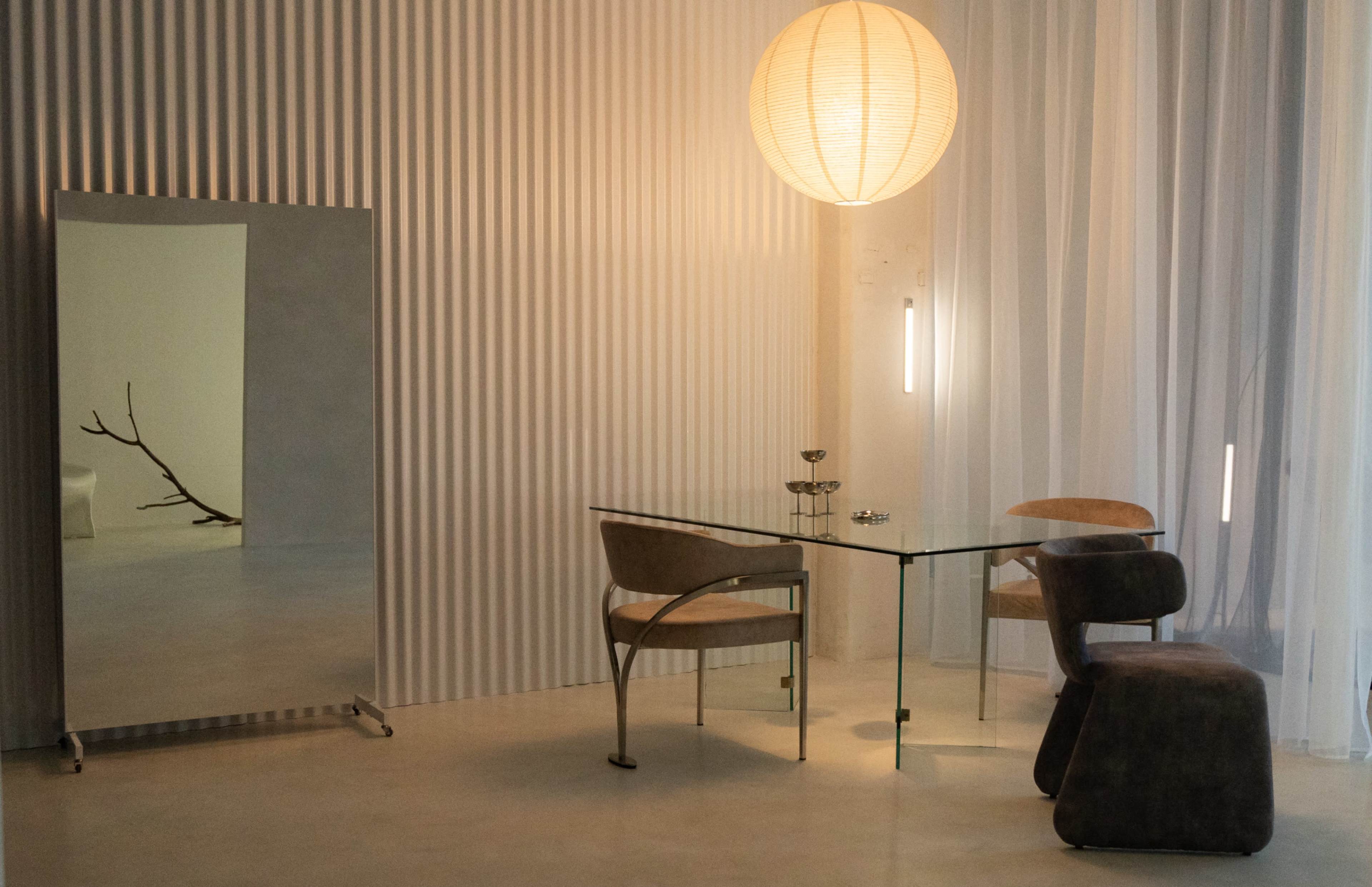 A modern dining area features a glass table with two chairs, a large mirror, and a round paper lantern hanging from the ceiling.