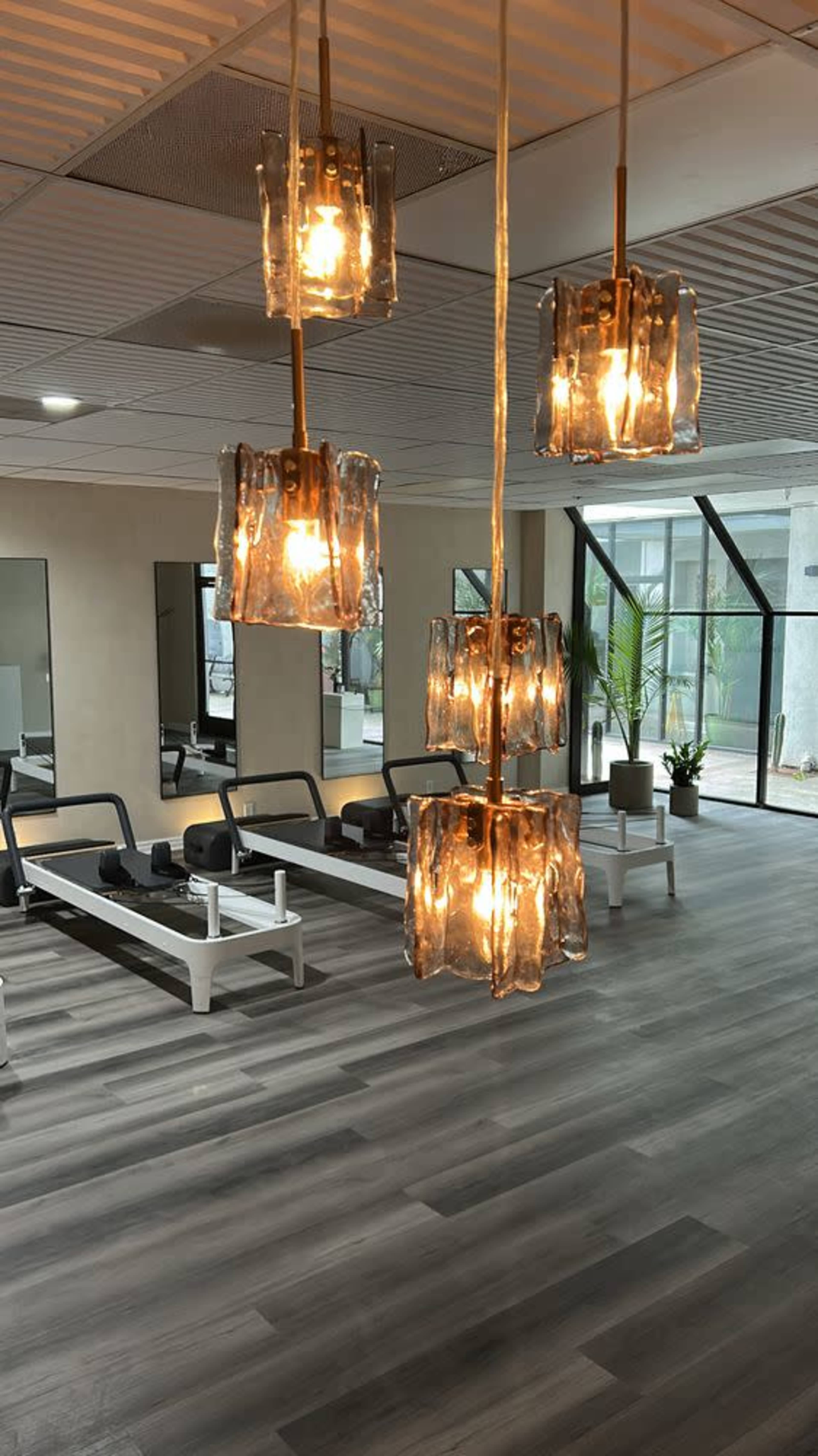 The image shows a modern indoor gym with stylish hanging lights, exercise equipment, and large mirrors on the walls.