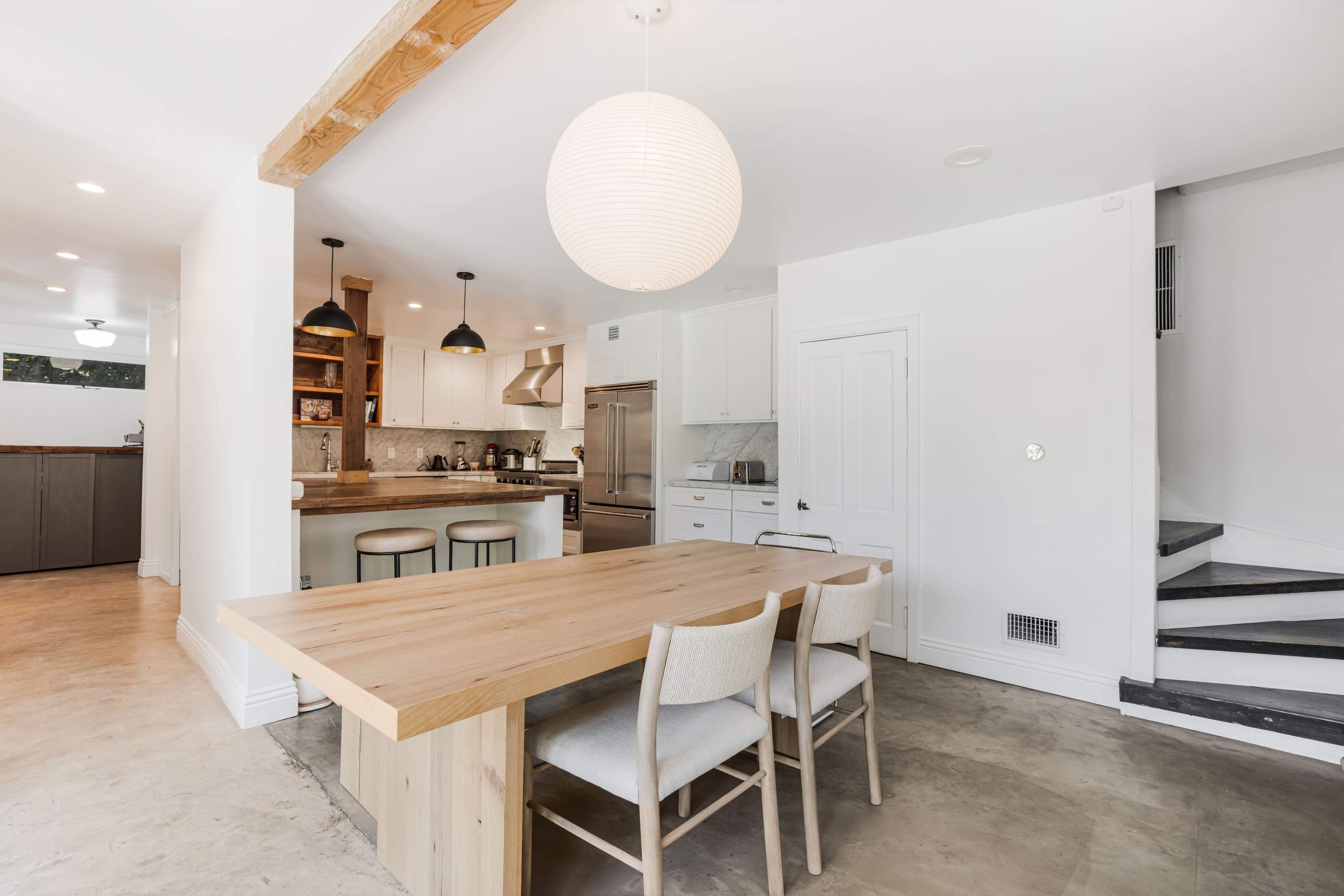 A modern kitchen features a wooden dining table with three chairs, an island with bar stools, and sleek cabinetry.