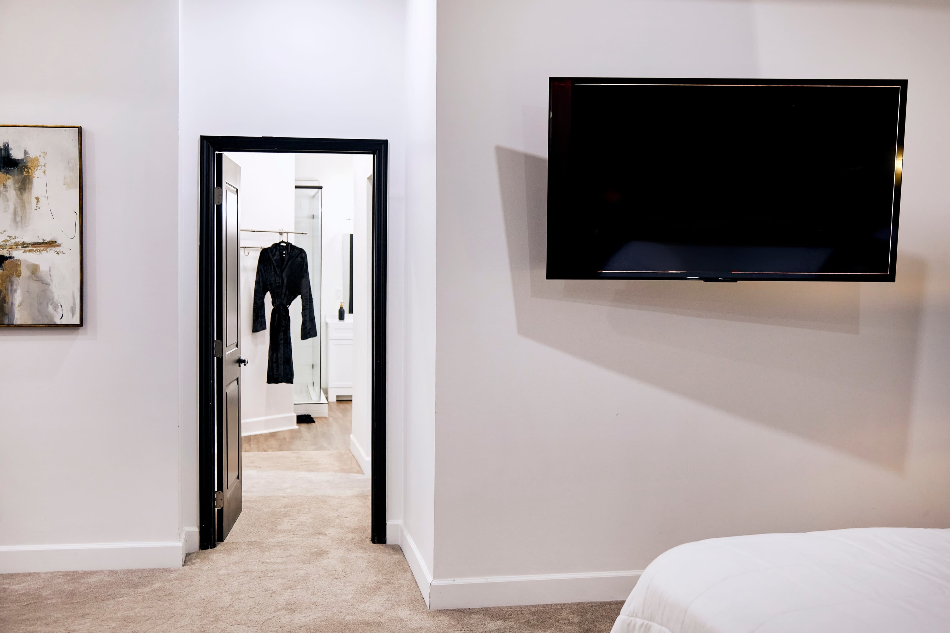 The image shows a bedroom with a television mounted on the wall and a doorway leading to a closet area that contains a hanging garment.
