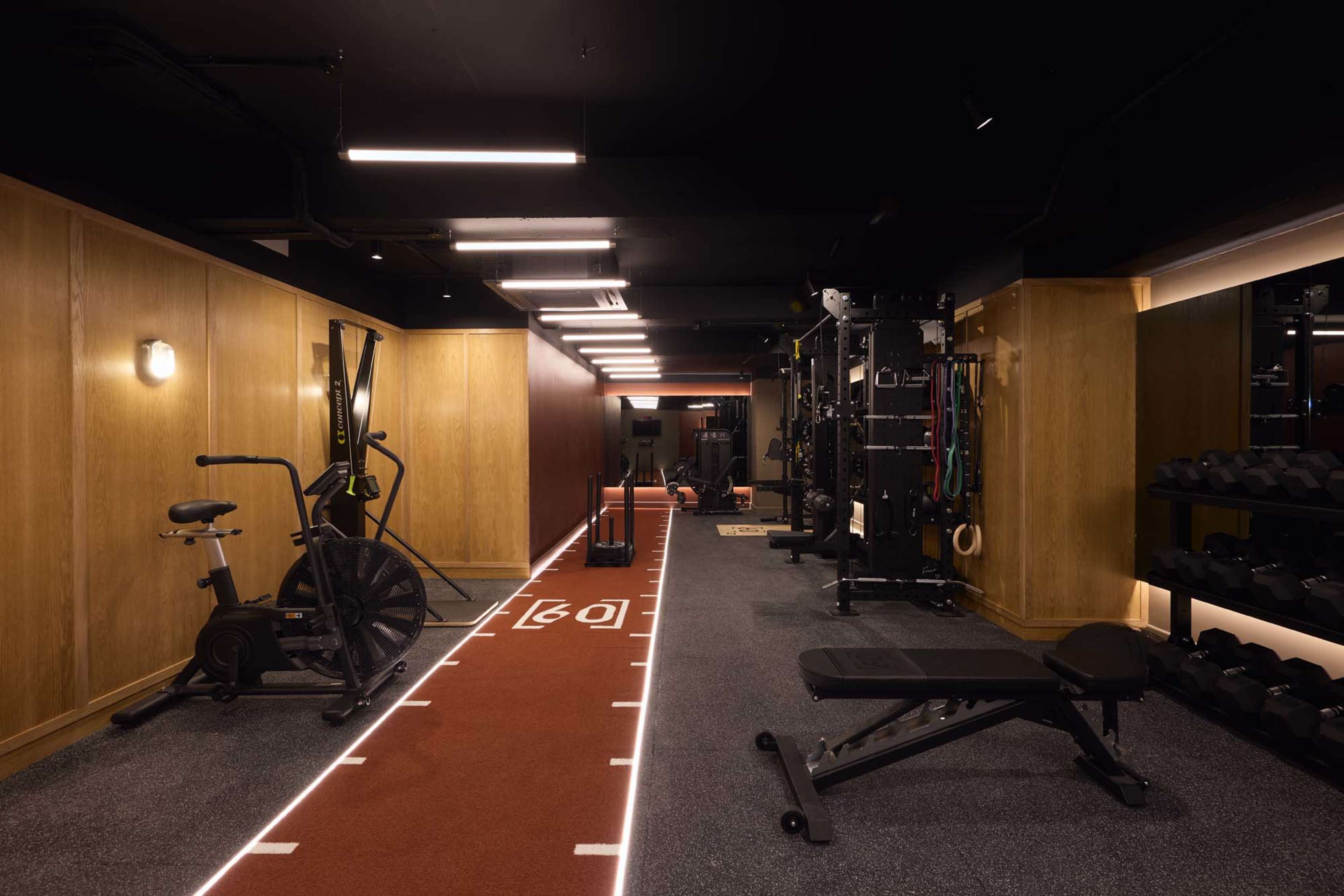 The image shows a modern gym interior featuring exercise equipment, including a stationary bike, weights, and a dedicated training area with a running track.