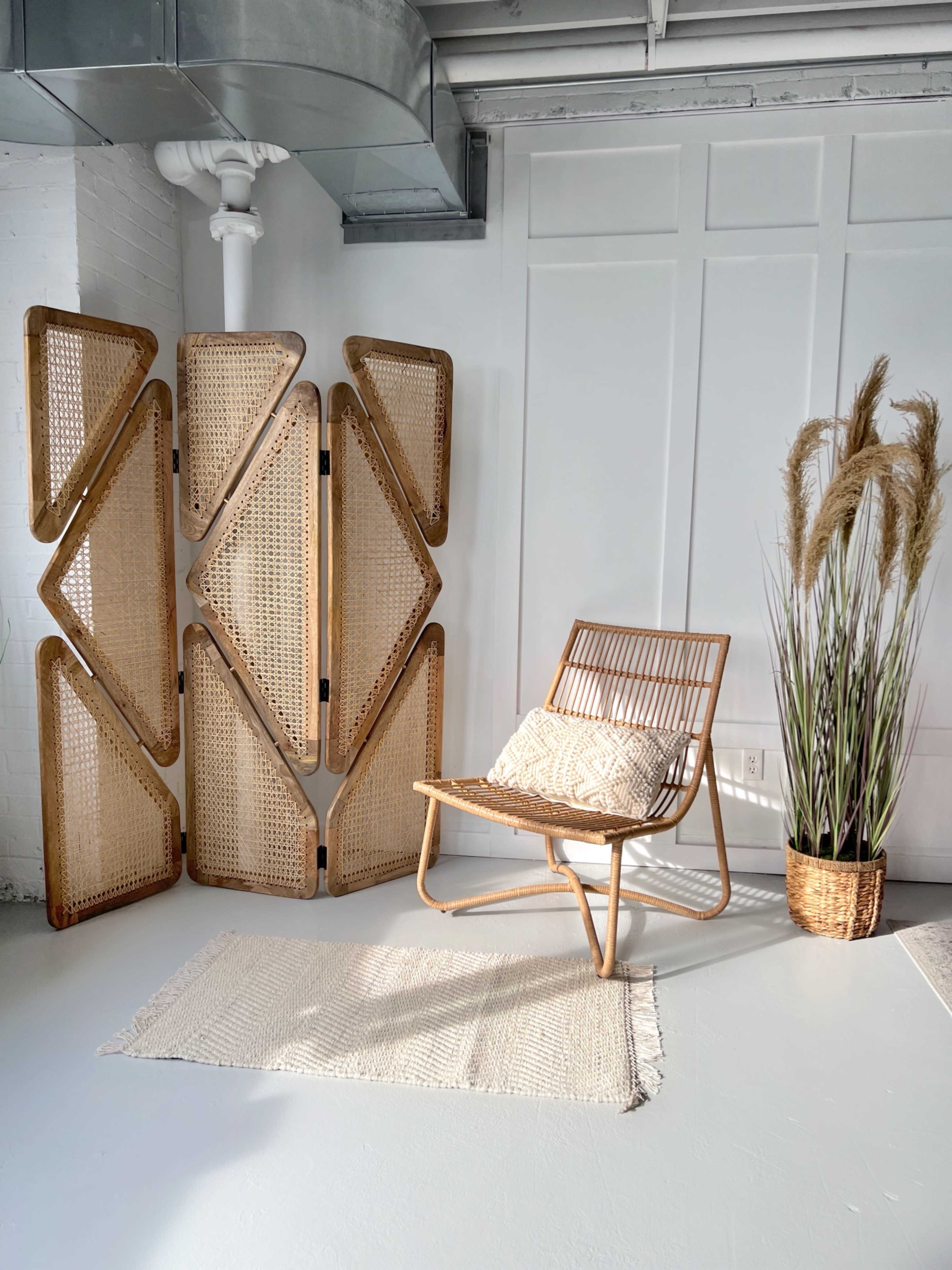 A rattan chair and a decorative screen stand beside a plant in a woven pot on a light-colored floor.