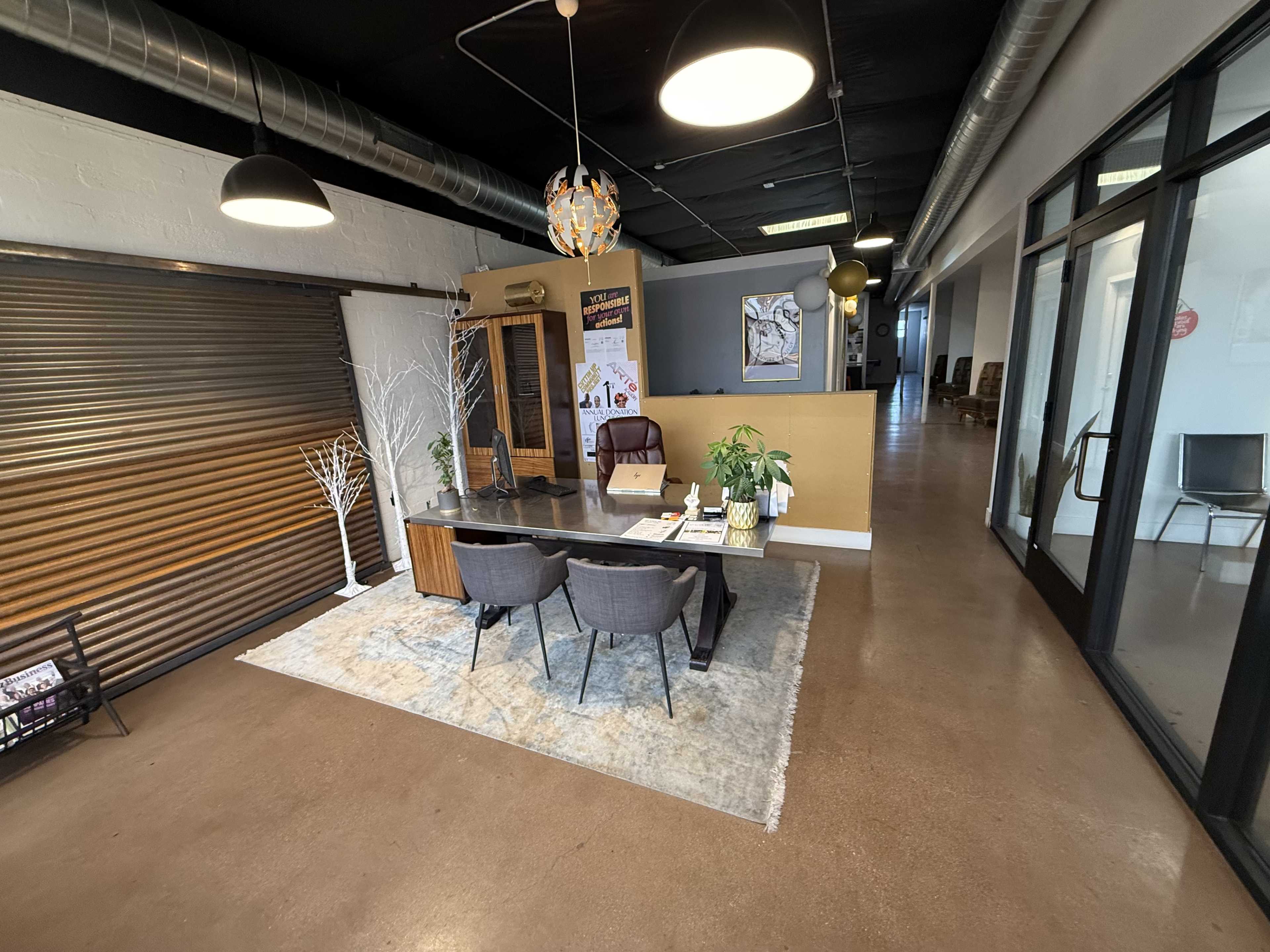 The image shows a modern office reception area with a desk, chairs, decorative plants, and a backdrop of sliding metal doors.