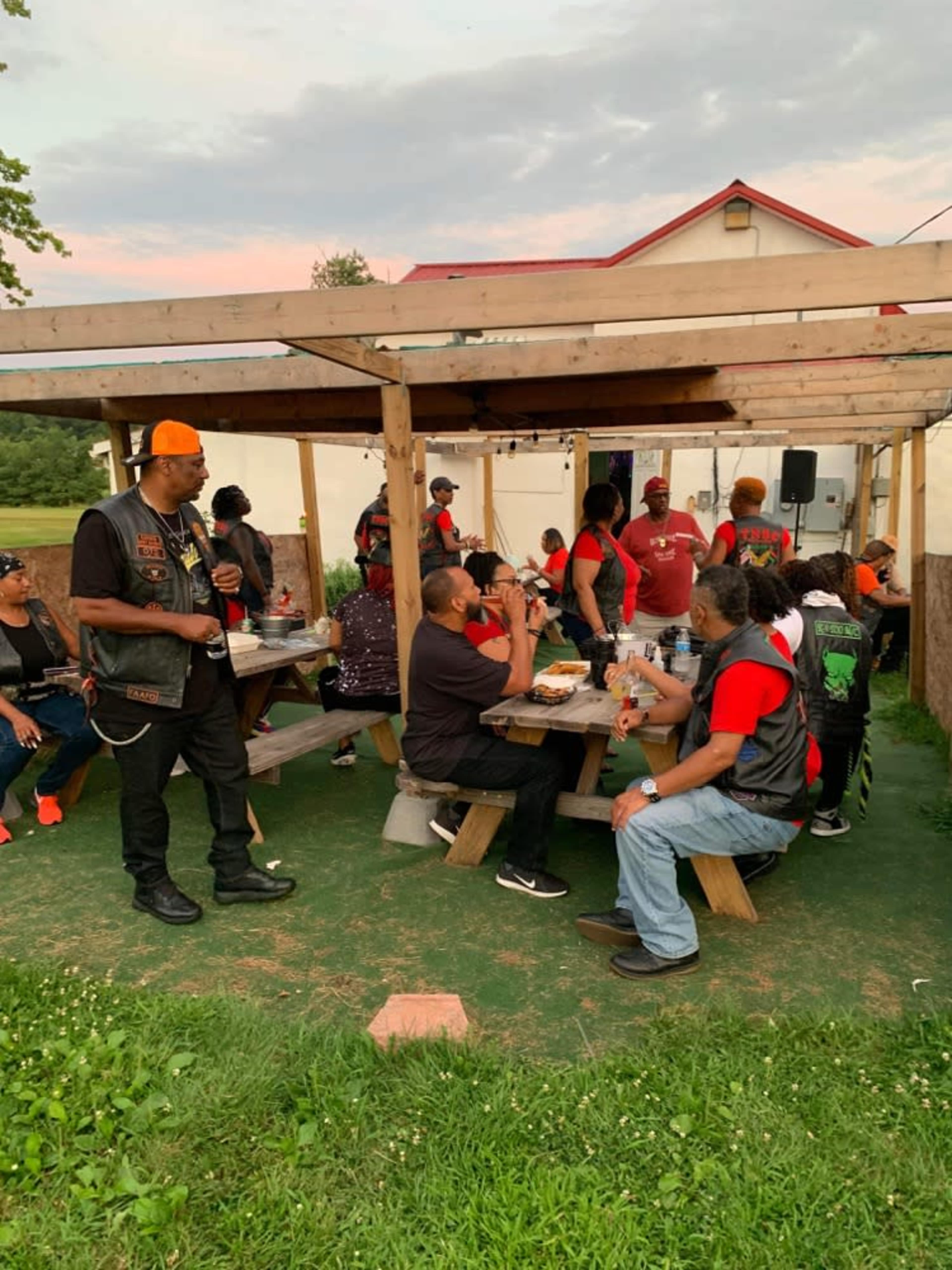 A group of people gathered under a wooden canopy, sharing food and drinks at a picnic area.