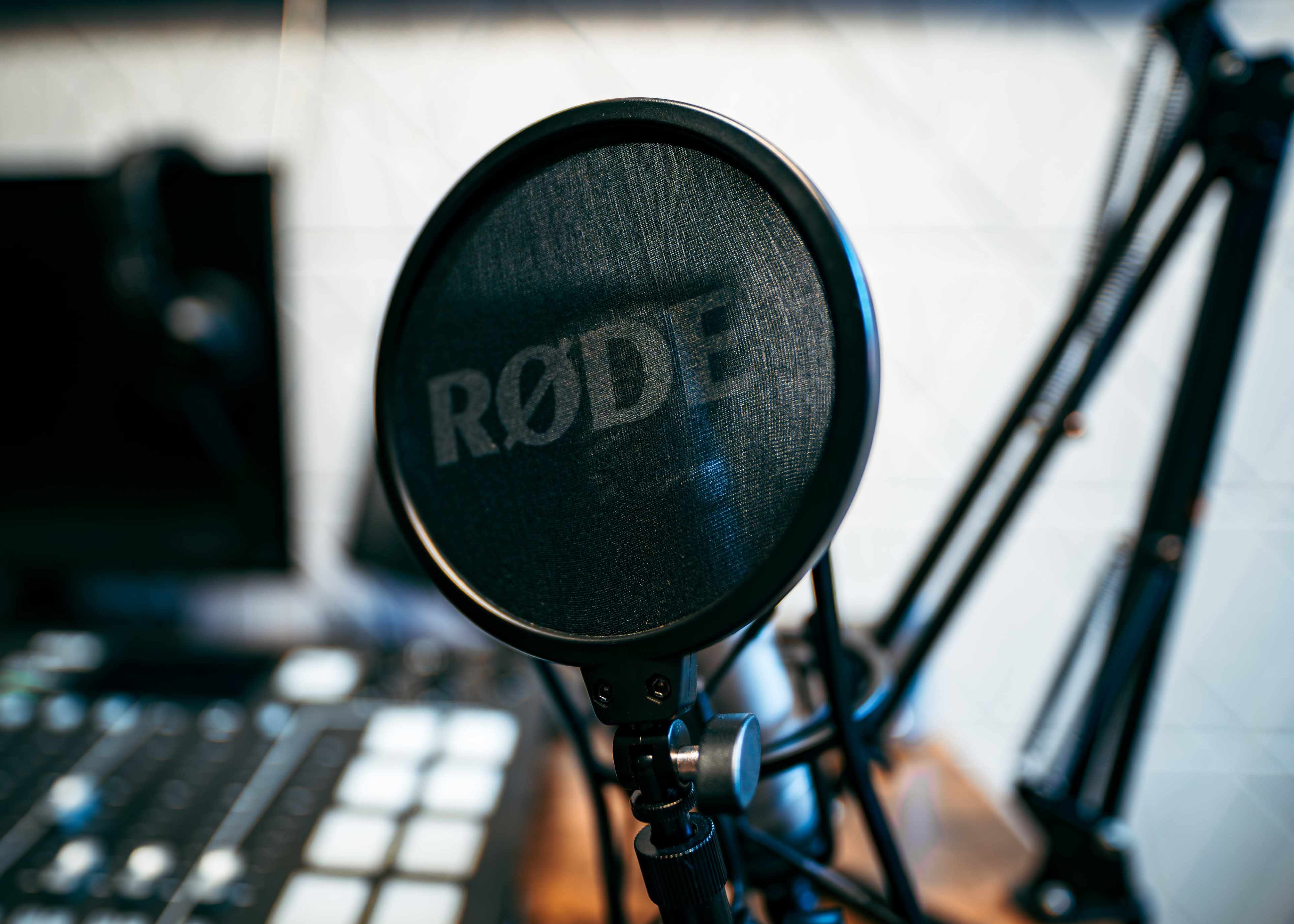 A close-up of a microphone with a pop filter, set against a backdrop of audio equipment.