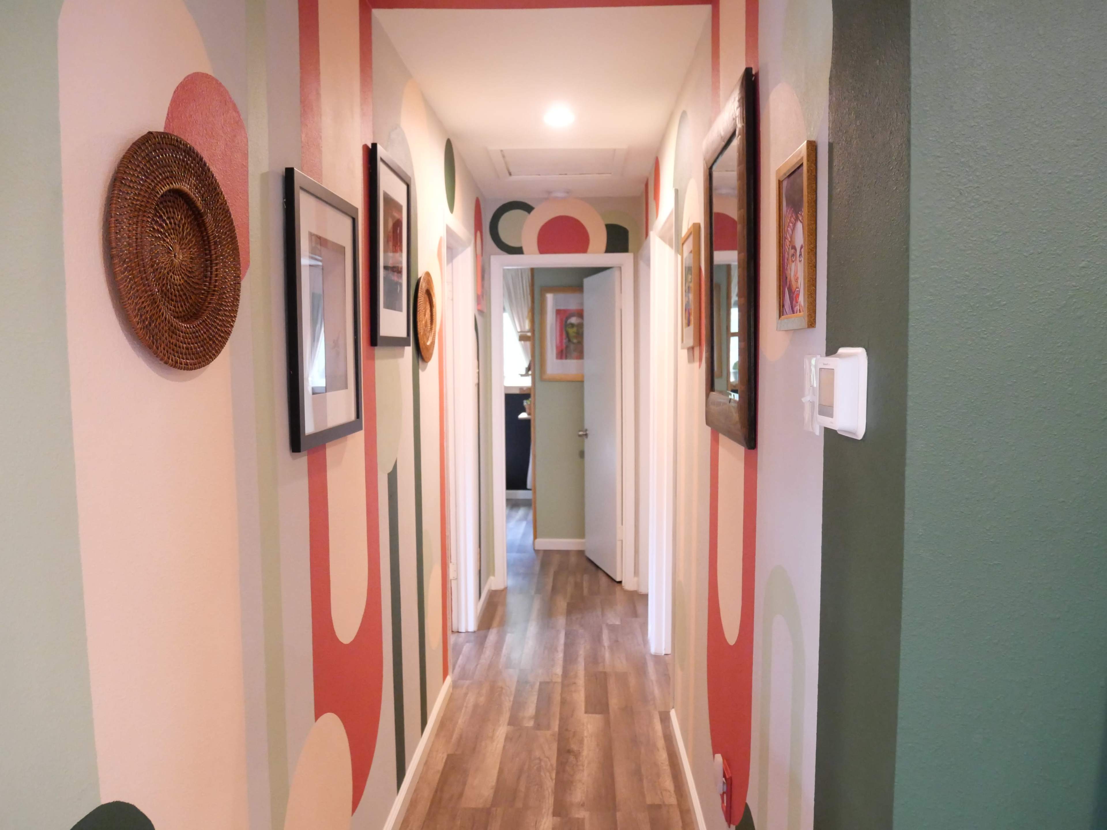 A hallway with patterned walls featuring circles and stripes, framed pictures, and decorative woven wall art.