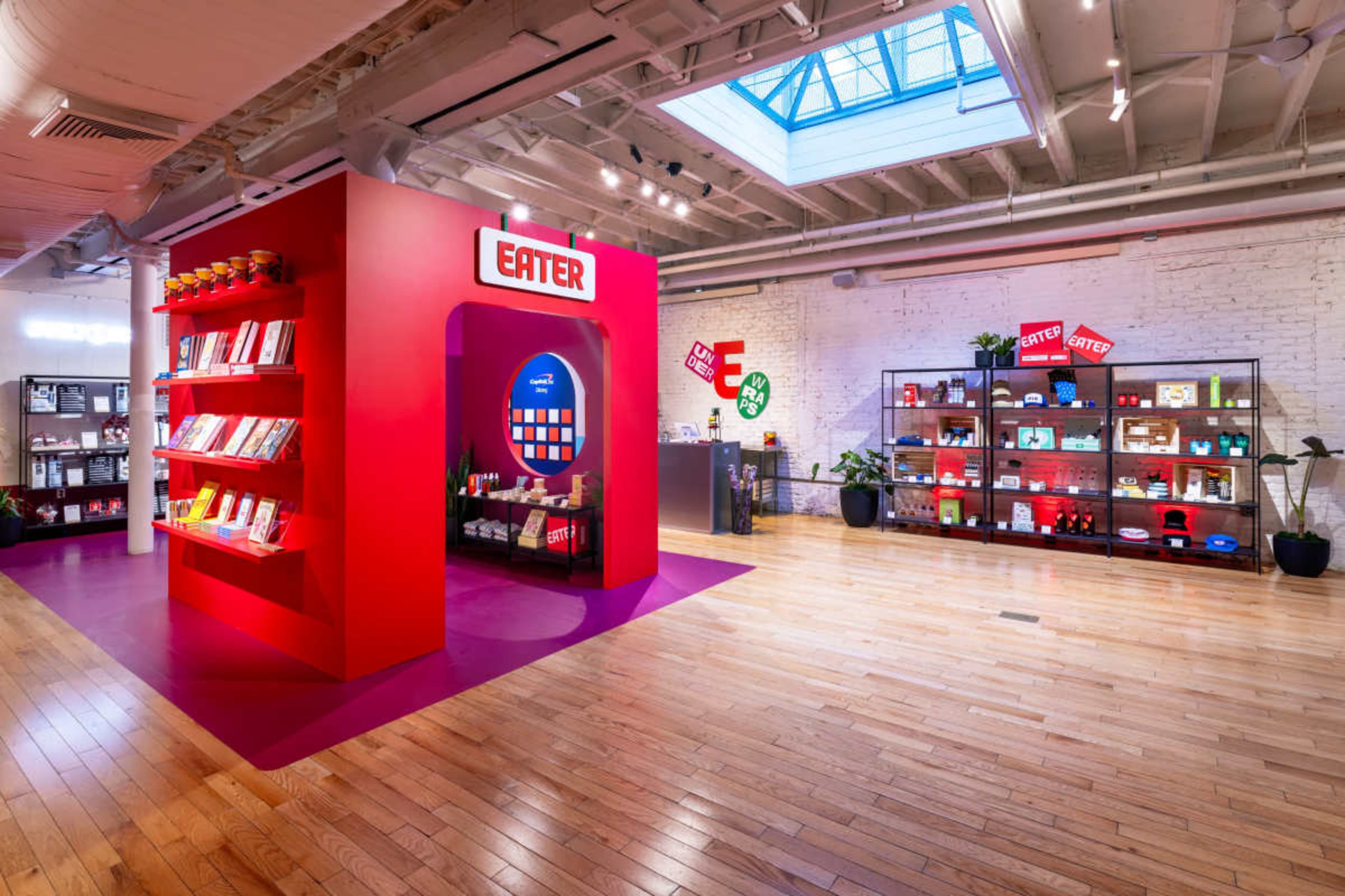 The image shows a brightly colored interior space featuring red walls, bookshelves filled with books and products, and a large circular display with the word "EATER."