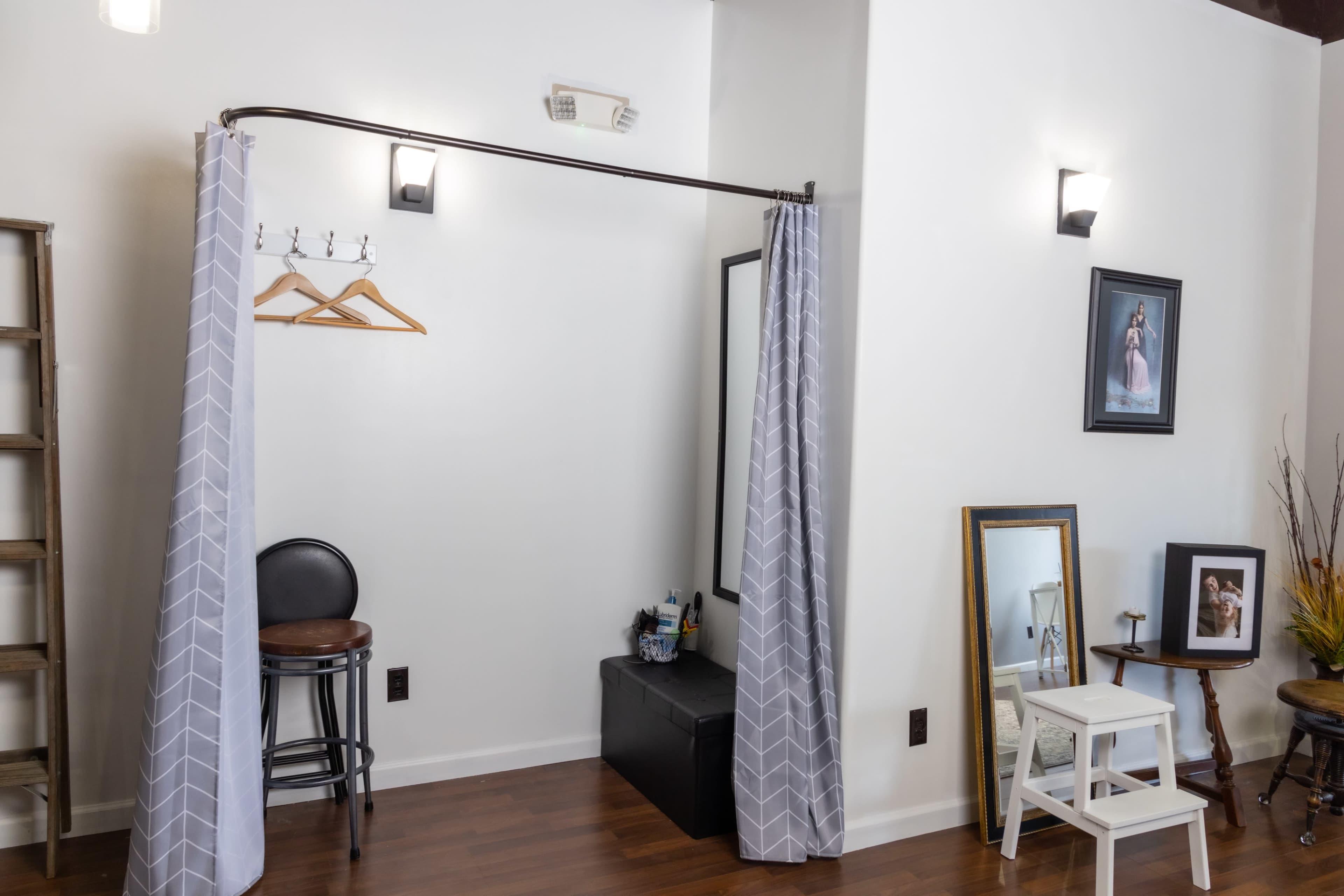 The image shows a fitting room area with a curtain, a stool, and several mirrors against a white wall.