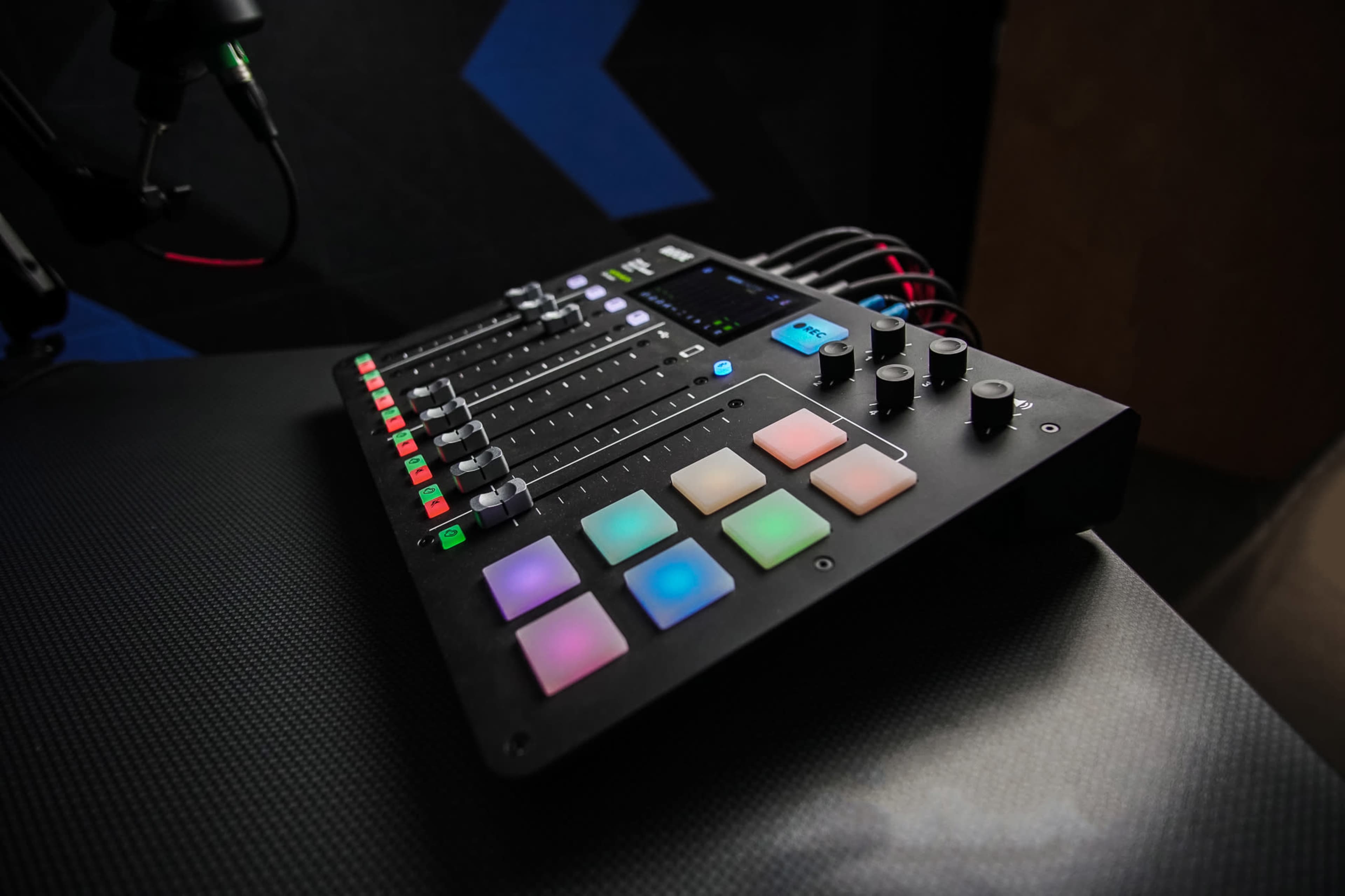 A digital audio mixer with multiple faders and colorful buttons is positioned on a textured surface.