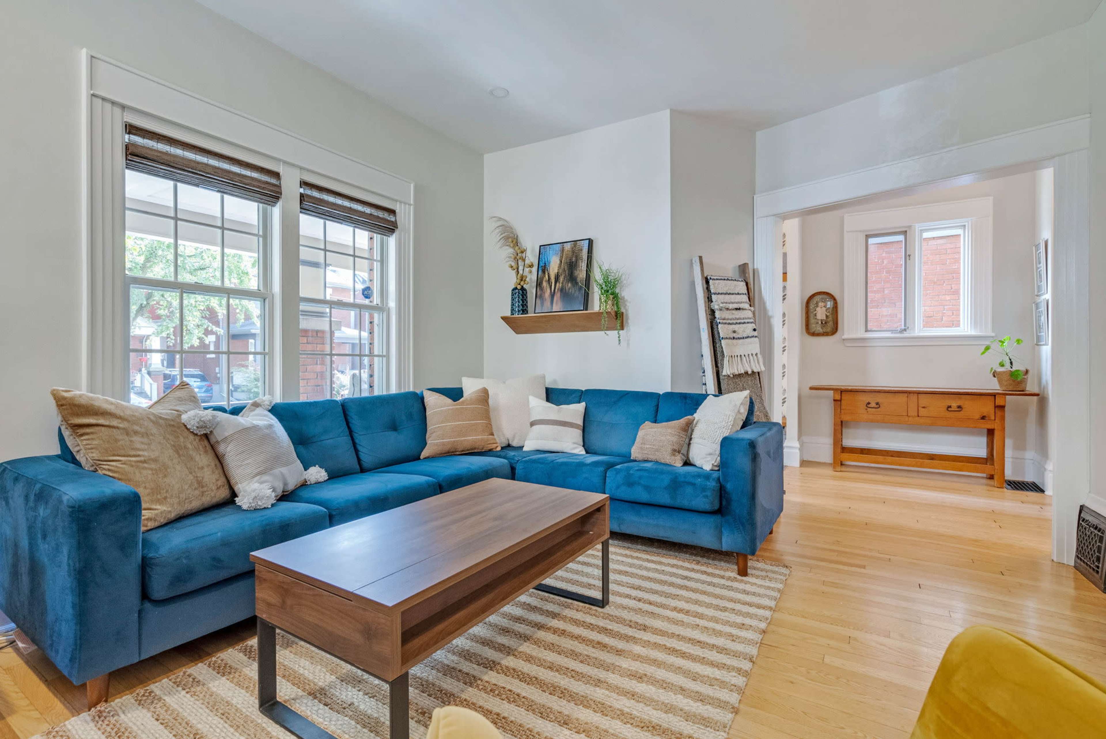The room features a blue sectional sofa arranged around a wooden coffee table, with natural light streaming through the large windows.