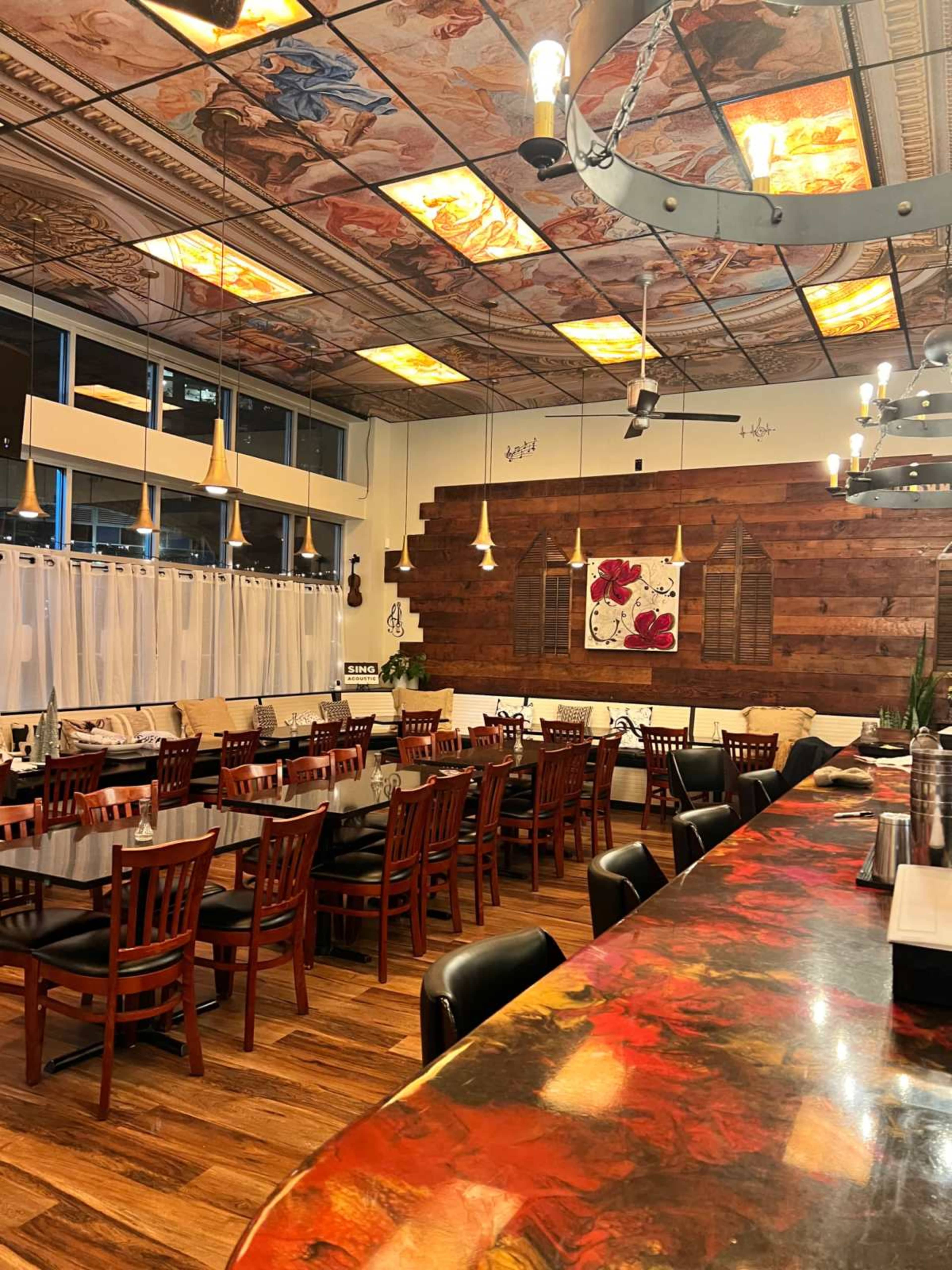 The image shows a modern restaurant interior with wooden furniture, decorative wall art, and a ceiling featuring intricate designs.