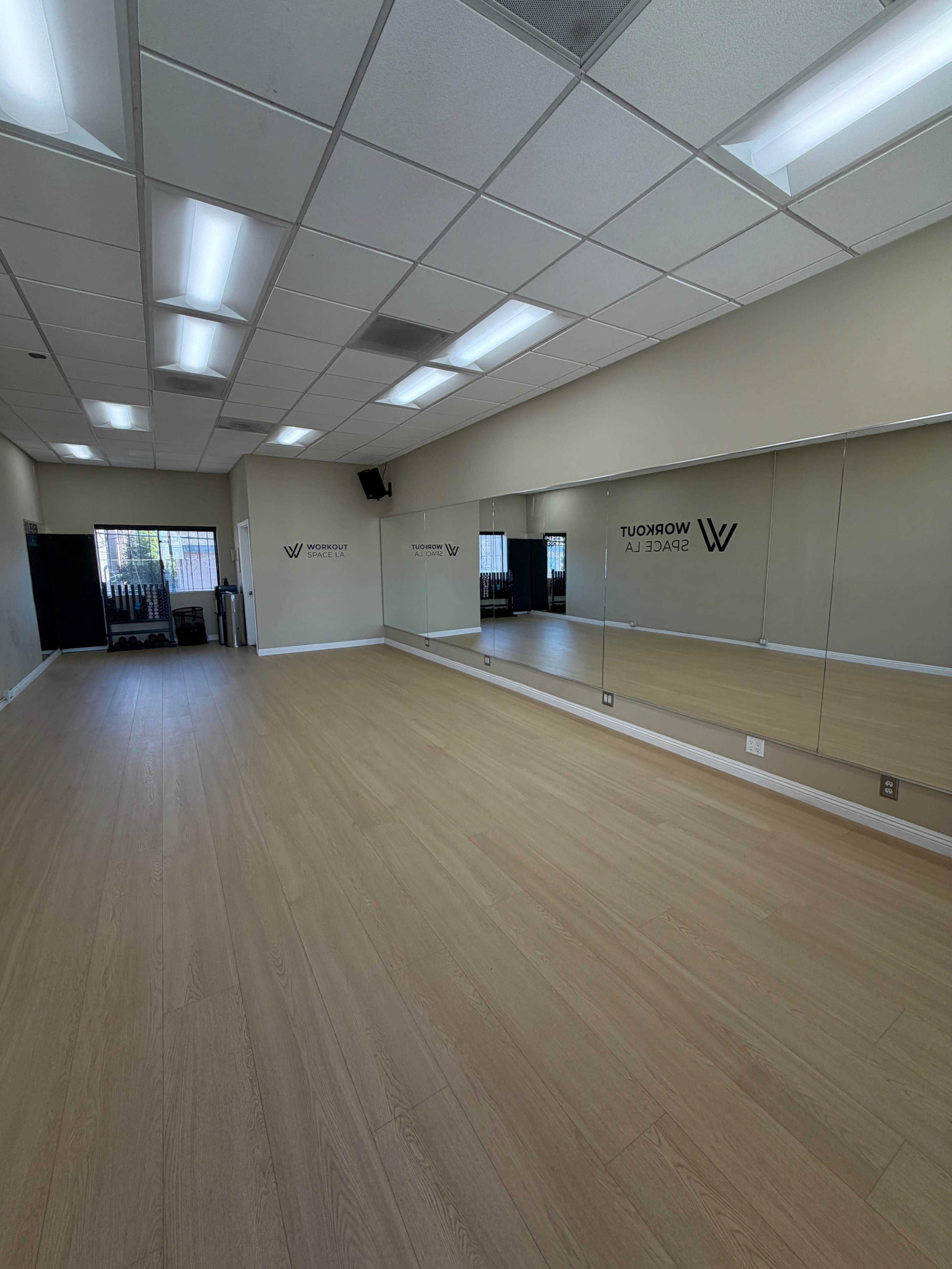 The image shows a spacious dance studio with wooden flooring and large mirrors along one wall.