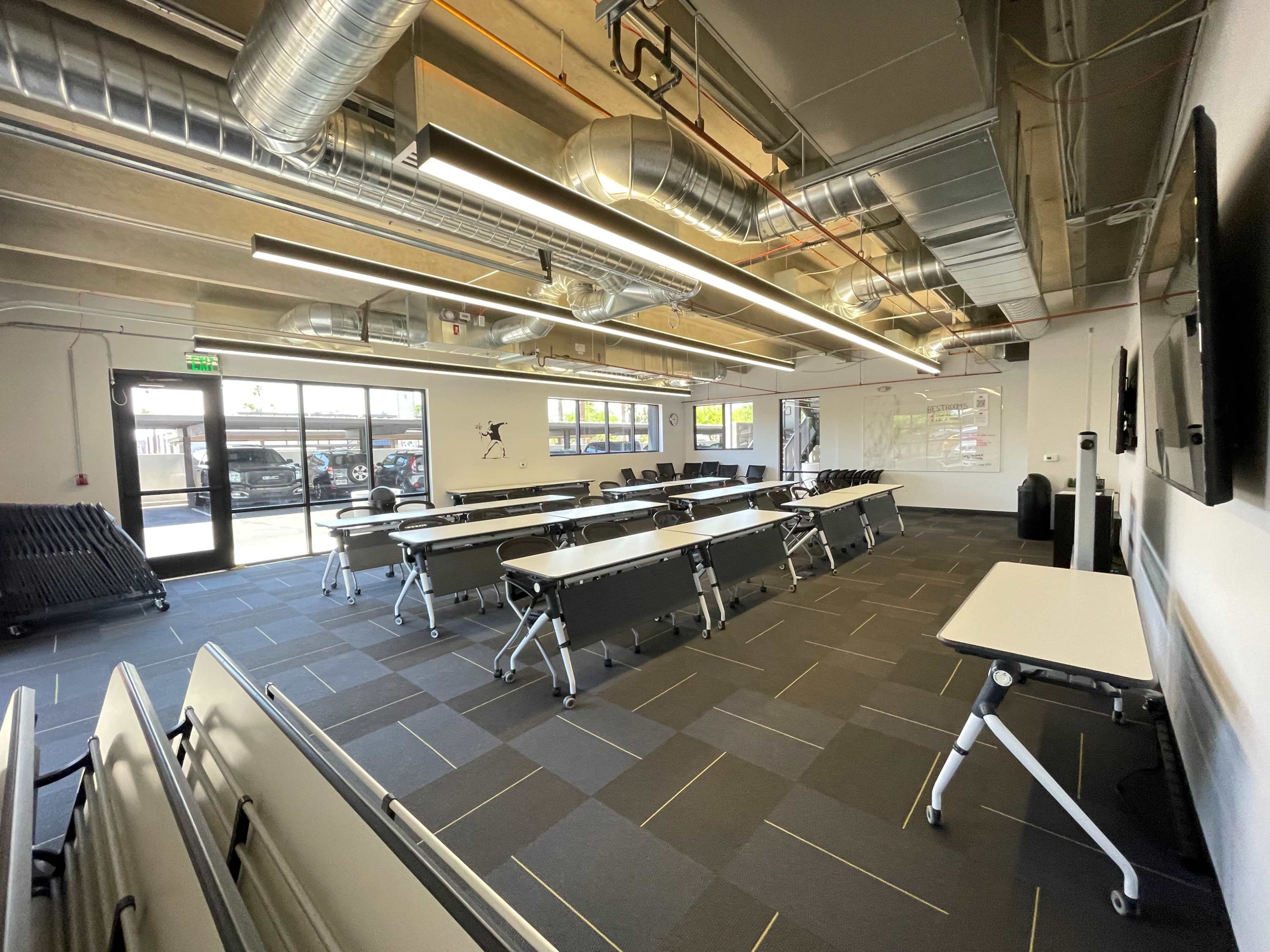 A modern classroom with movable tables arranged in a spacious layout under a ceiling with exposed ductwork.