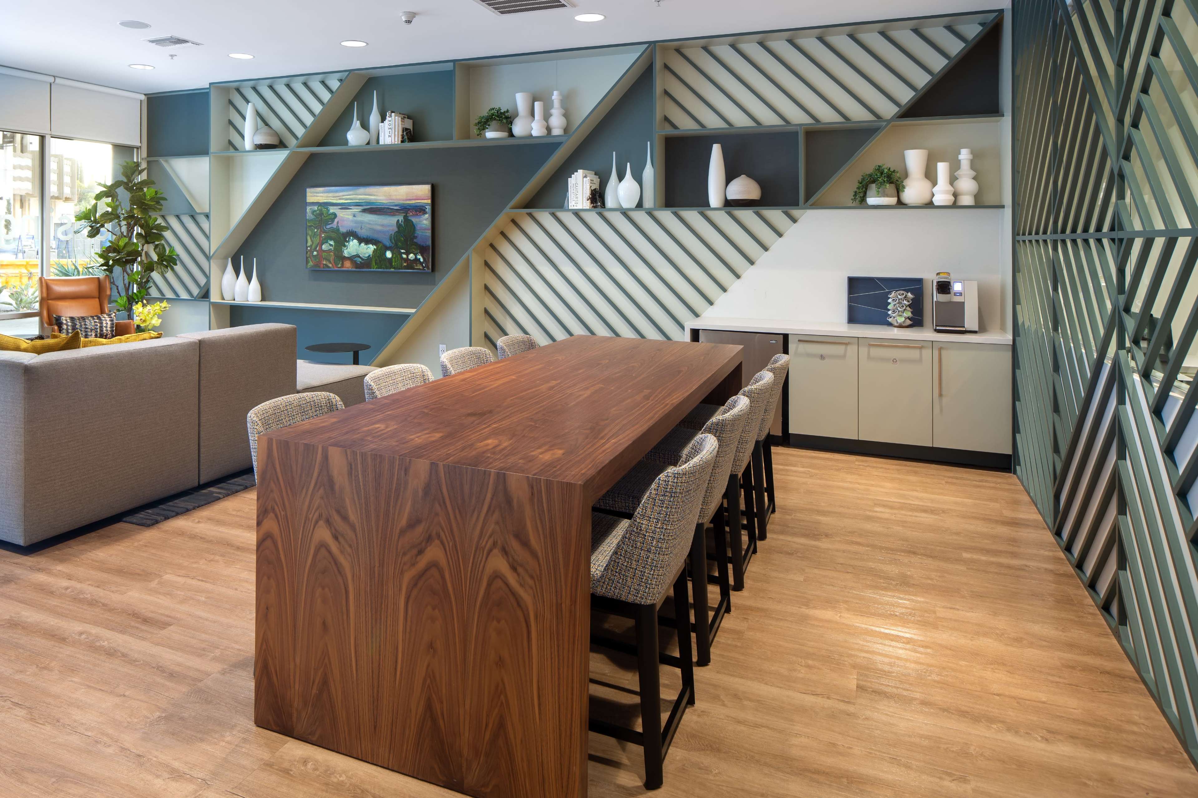 A modern kitchen and dining area featuring a long wooden table with high chairs, alongside a sleek cabinetry and decorative shelving on the walls.