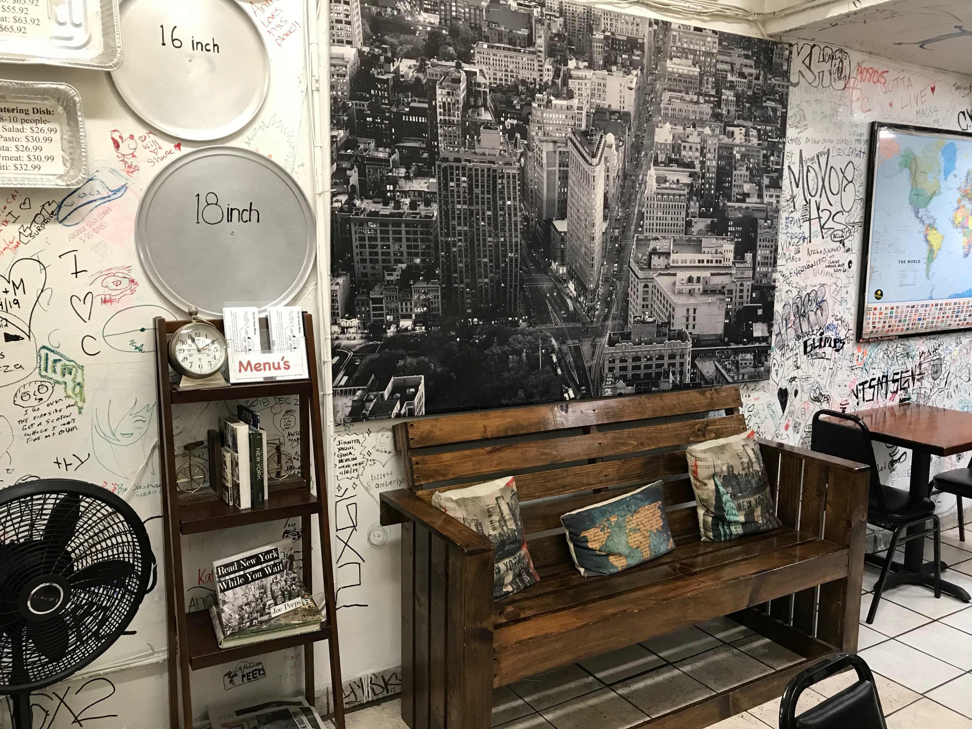 The image shows a cozy eatery with a wooden bench, a large black-and-white cityscape photo on the wall, and graffiti-covered walls.