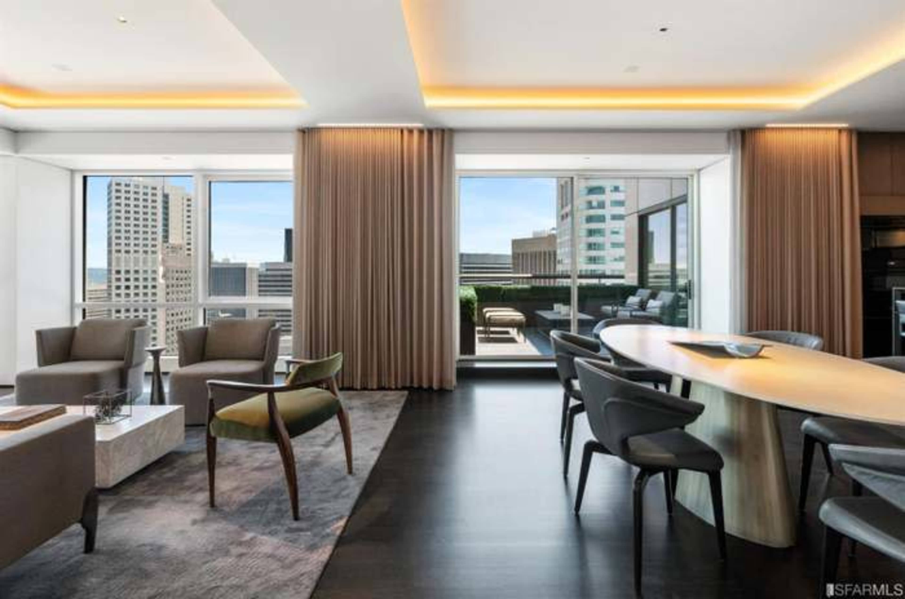 A modern living space features a seating area with two chairs, a round dining table, and large windows overlooking a cityscape.