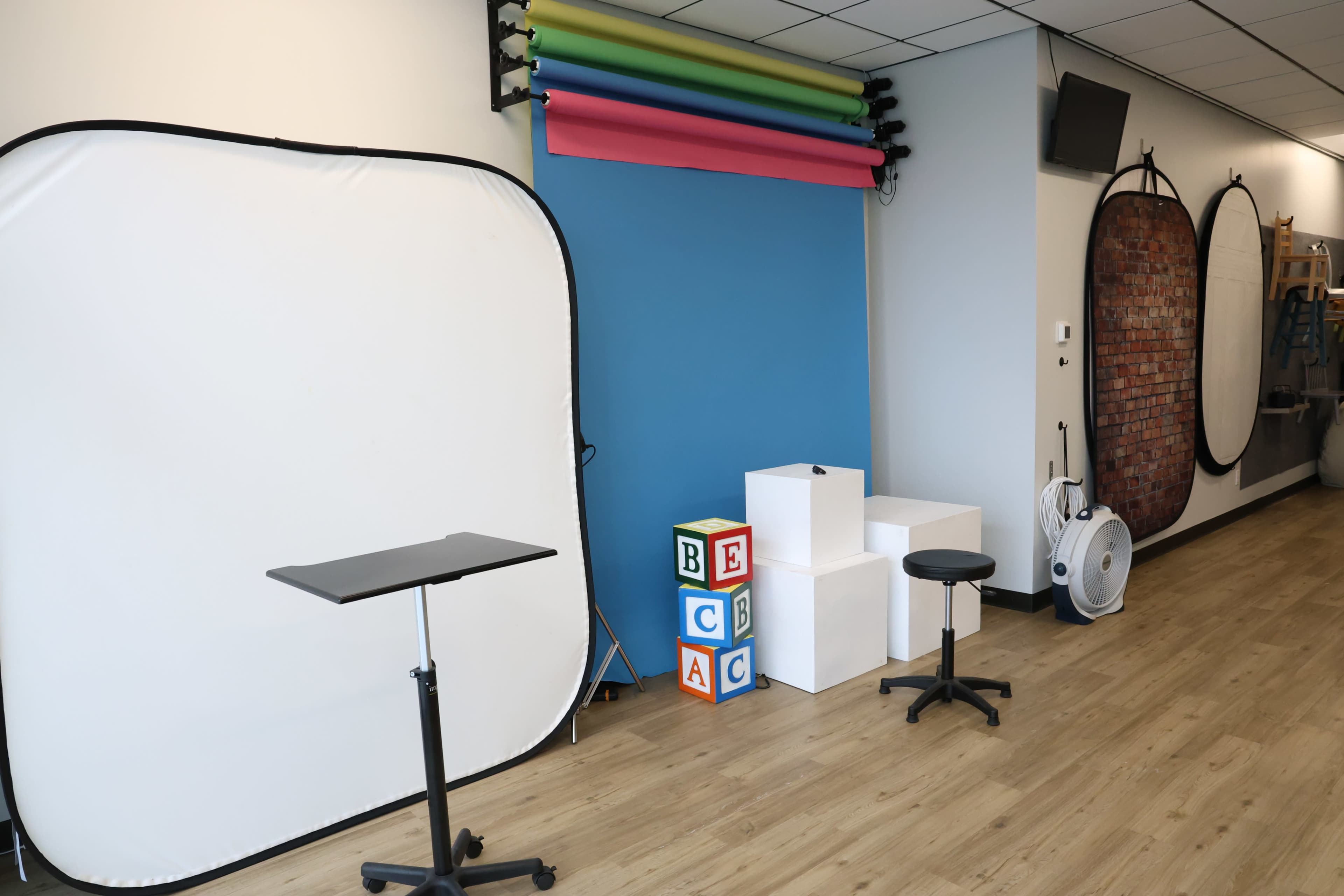 A studio setup with a white backdrop, colorful paper rolls, decorative blocks, and two stools arranged in a well-lit room.