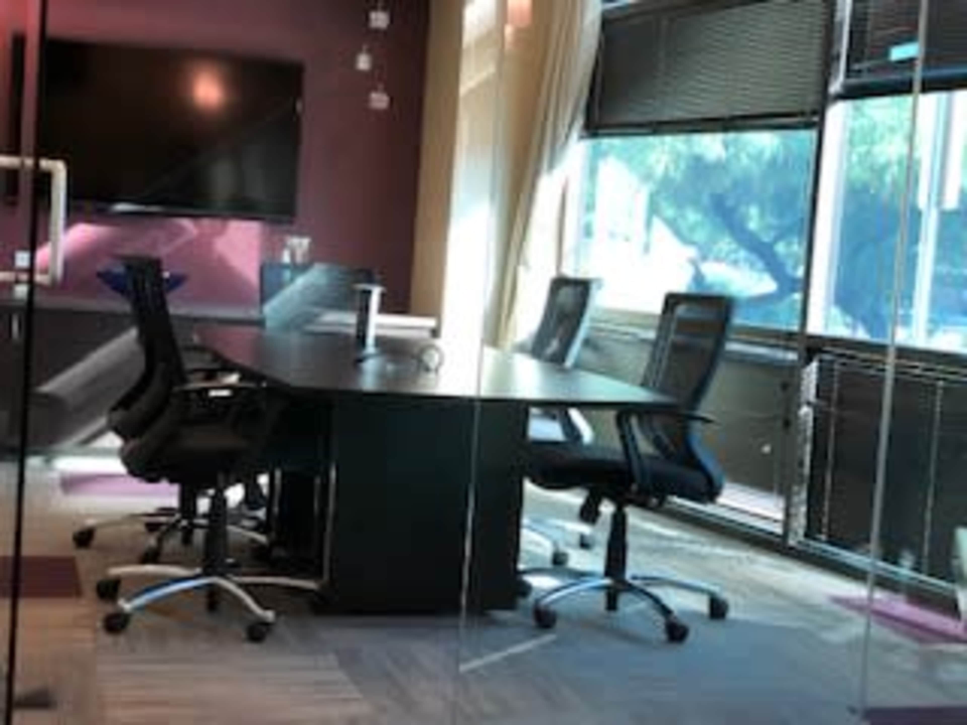 A modern conference room with a large table surrounded by several office chairs and a large screen mounted on the wall.