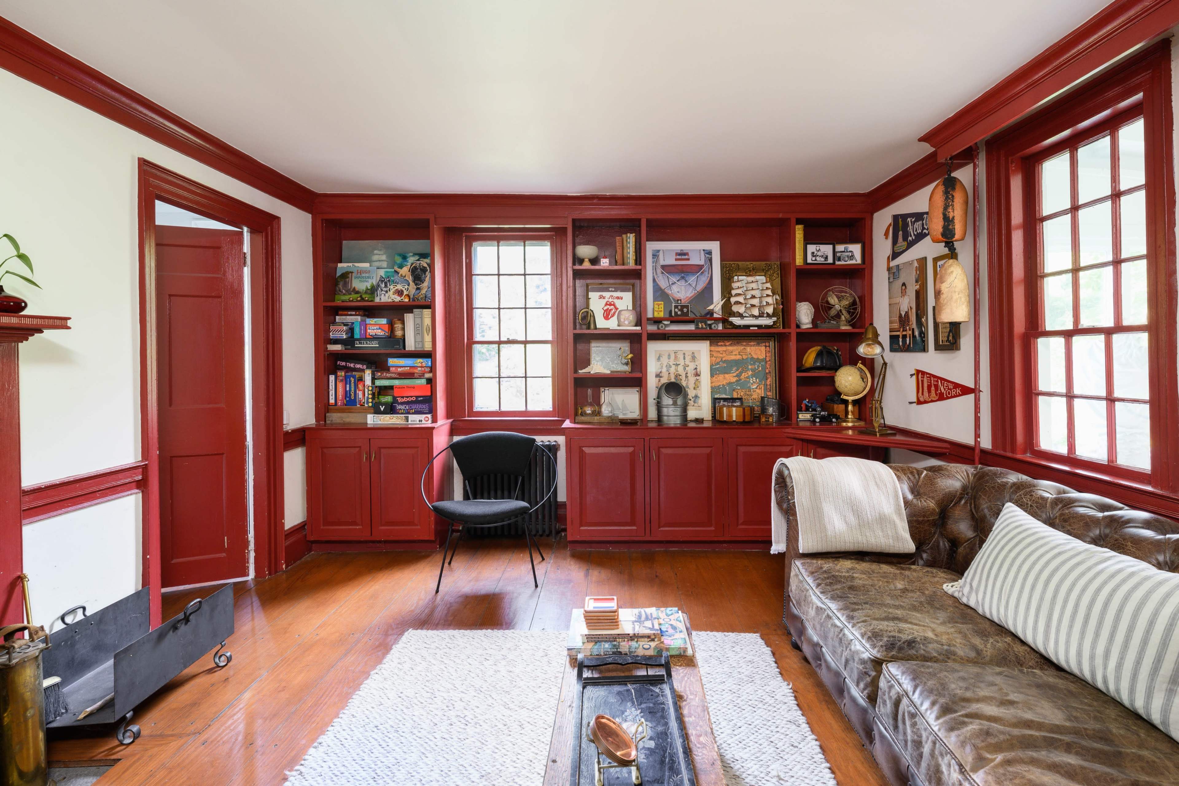 The image shows a cozy living room with red walls, a brown leather couch, a black armchair, and built-in shelves filled with various books and decor.